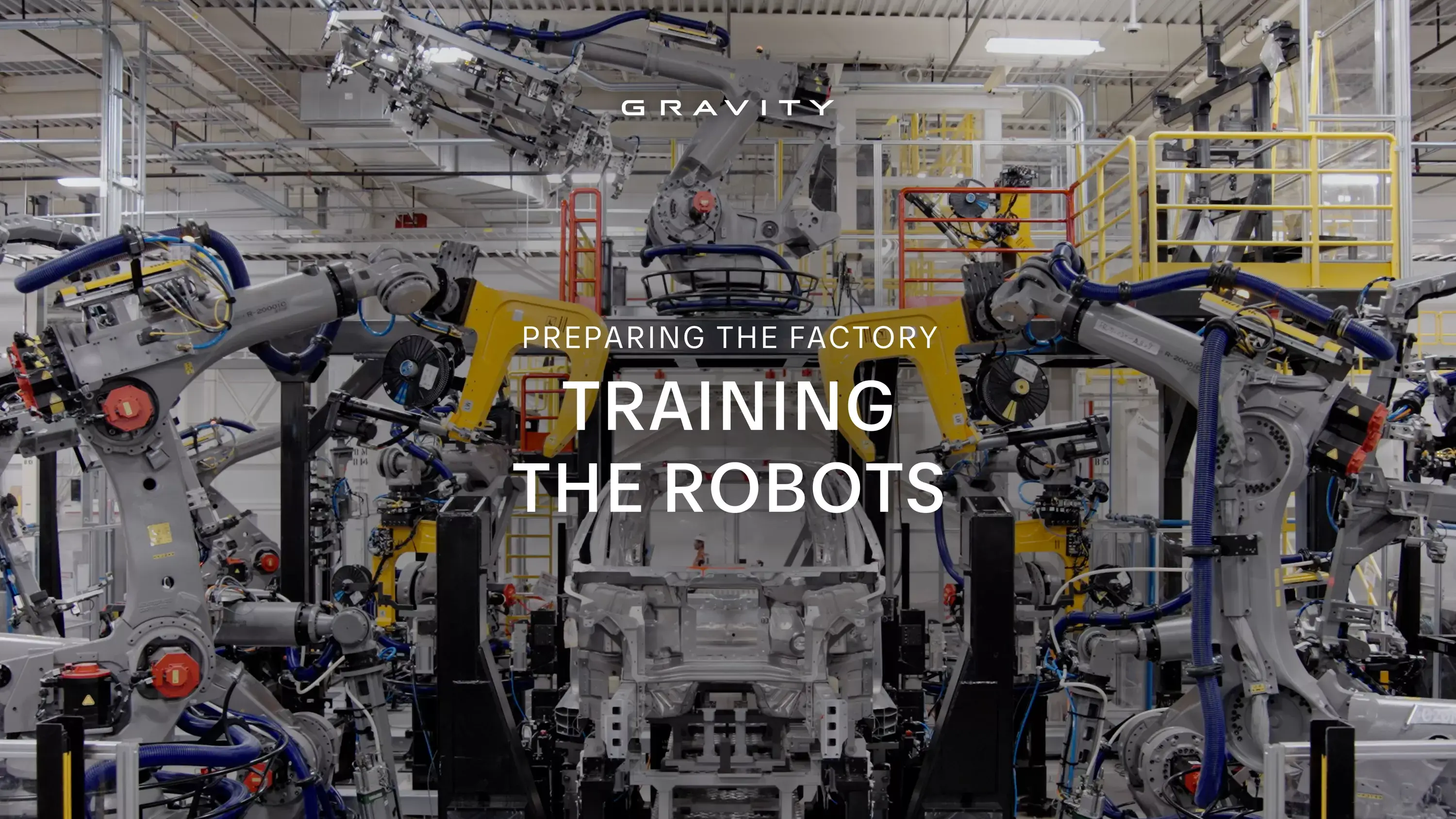 Industrial robotic arms surrounding a vehicle frame in a Gravity factory with text "TRAINING THE ROBOTS" overlaid.