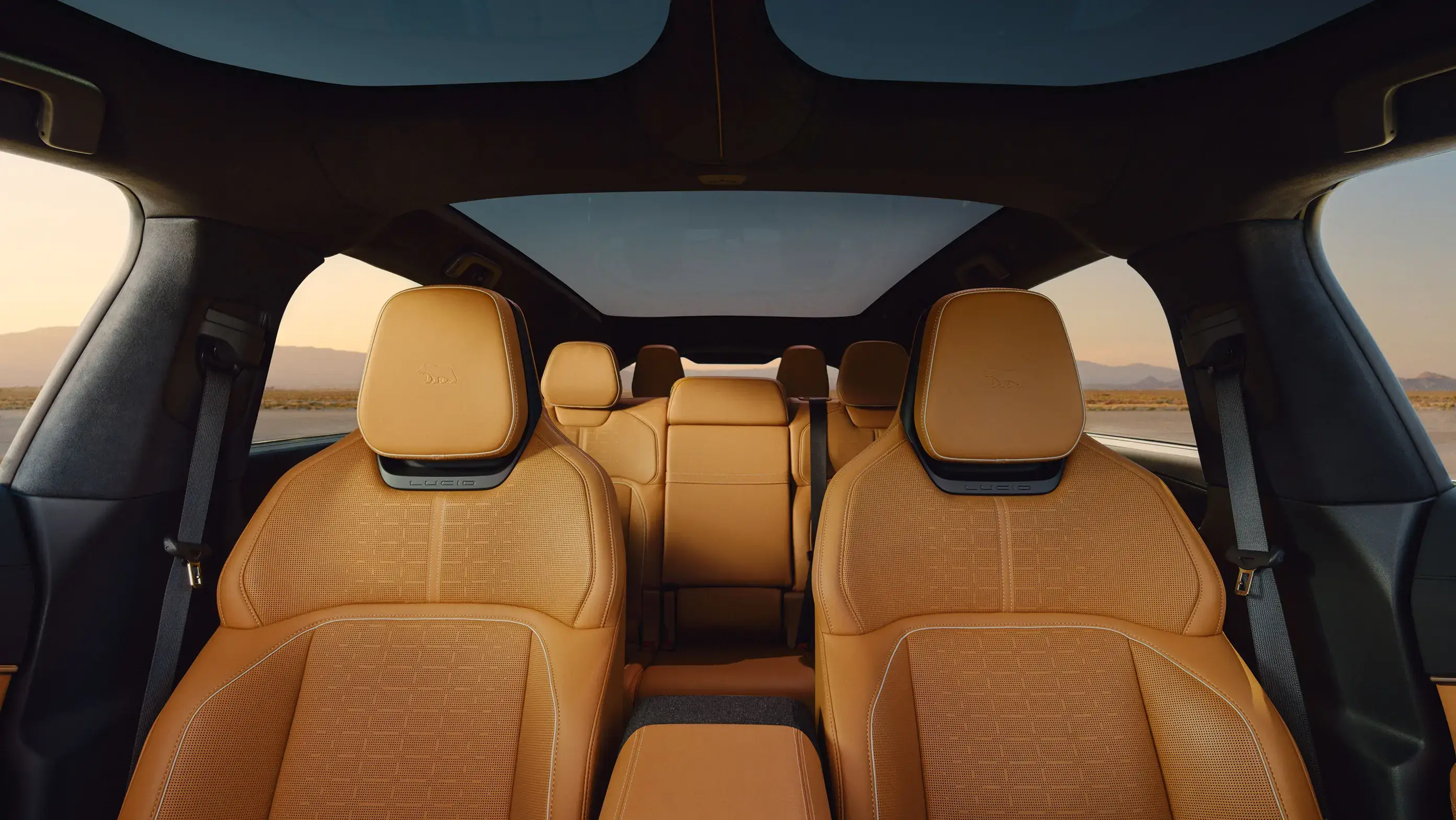 Luxury SUV interior with tan leather seats, panoramic sunroof, and desert landscape visible through windows at sunset.
