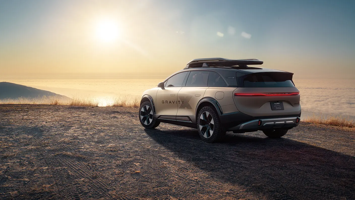 Lucid Gravity electric SUV parked on cliff overlooking ocean at sunset, with roof rack and distinctive taillight design.