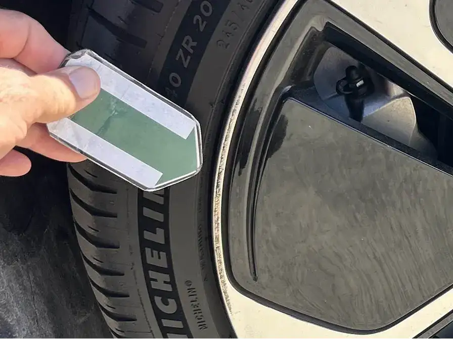 Hand holding a small green device near a car tire with Michelin branding visible on the sidewall.