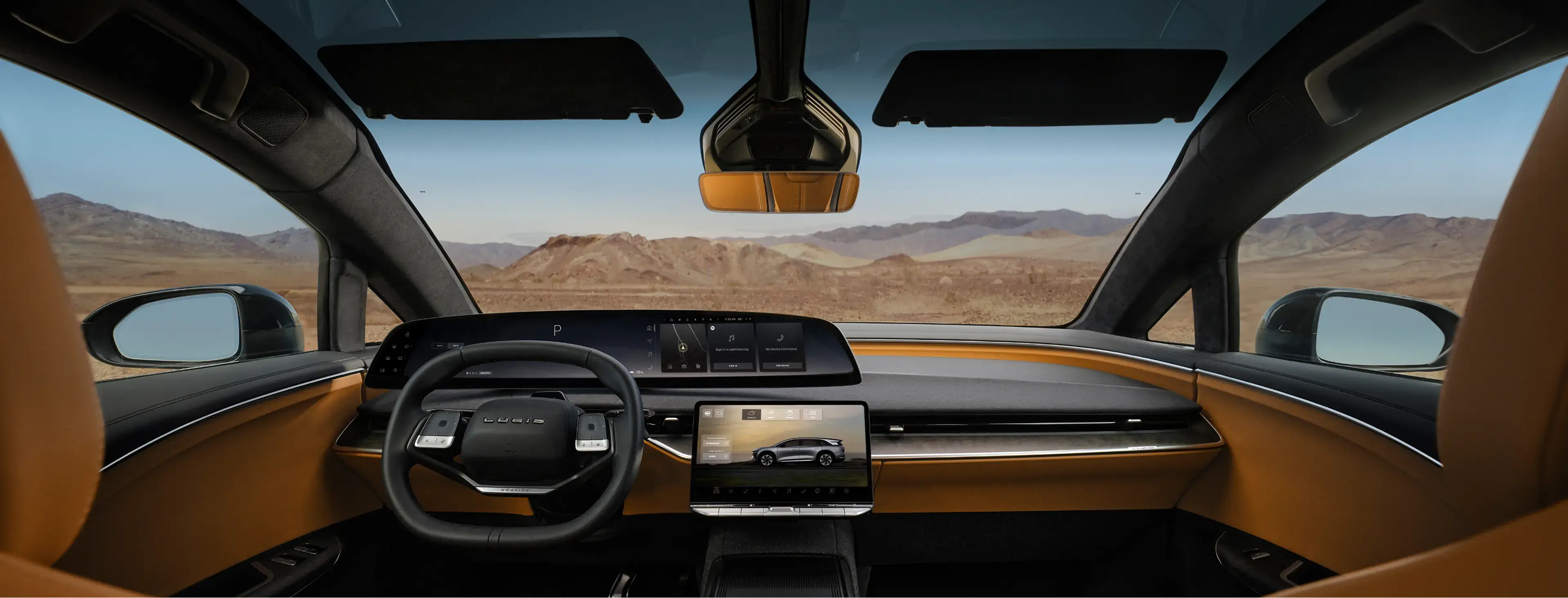 Lucid car interior with black steering wheel, dual touchscreens, amber trim, and a desert mountain landscape through the windshield.
