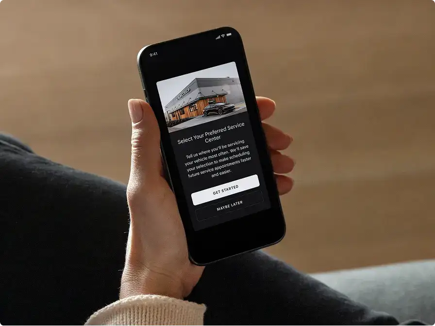 Hand holding a smartphone displaying a "Select Your Preferred Service Center" screen with a "Get Started" button.