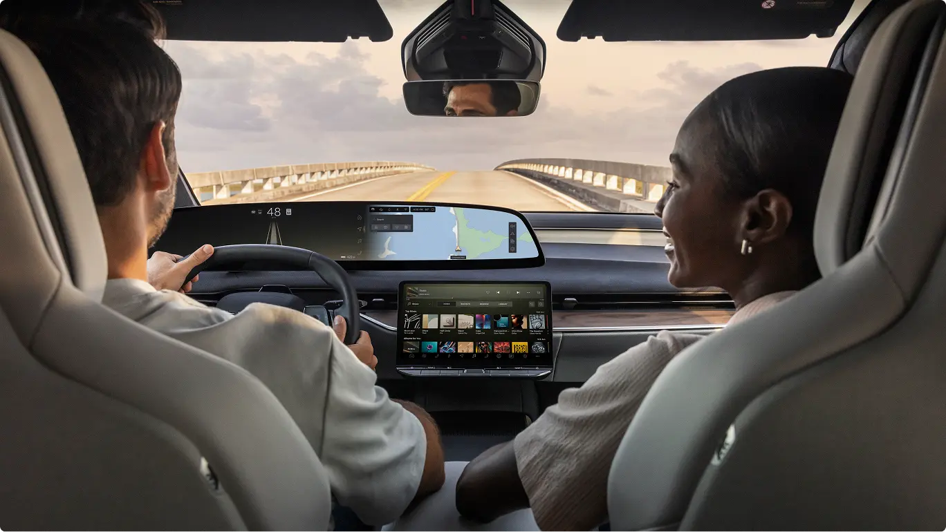 Two people driving on a bridge in a Lucid Gravity with digital displays showing navigation and entertainment options.