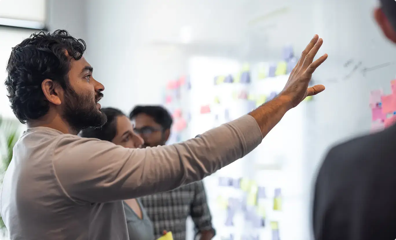 Person with curly hair gesturing at whiteboard during collaborative meeting in bright office space