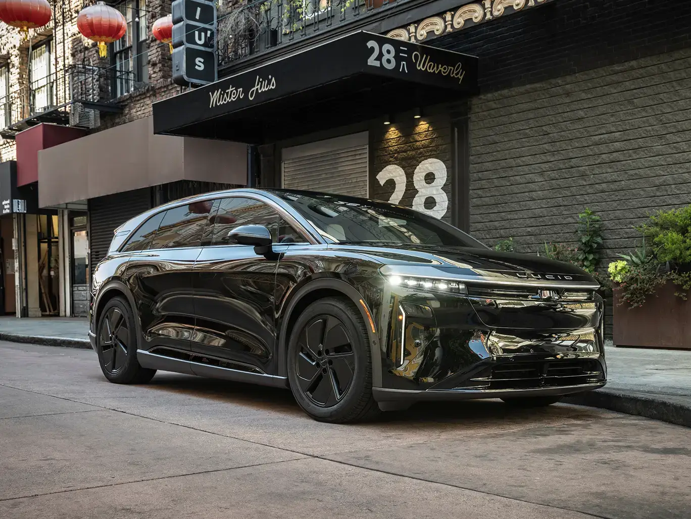 A sleek black SUV parked on a city street in front of a building numbered 28, with red lanterns visible above.