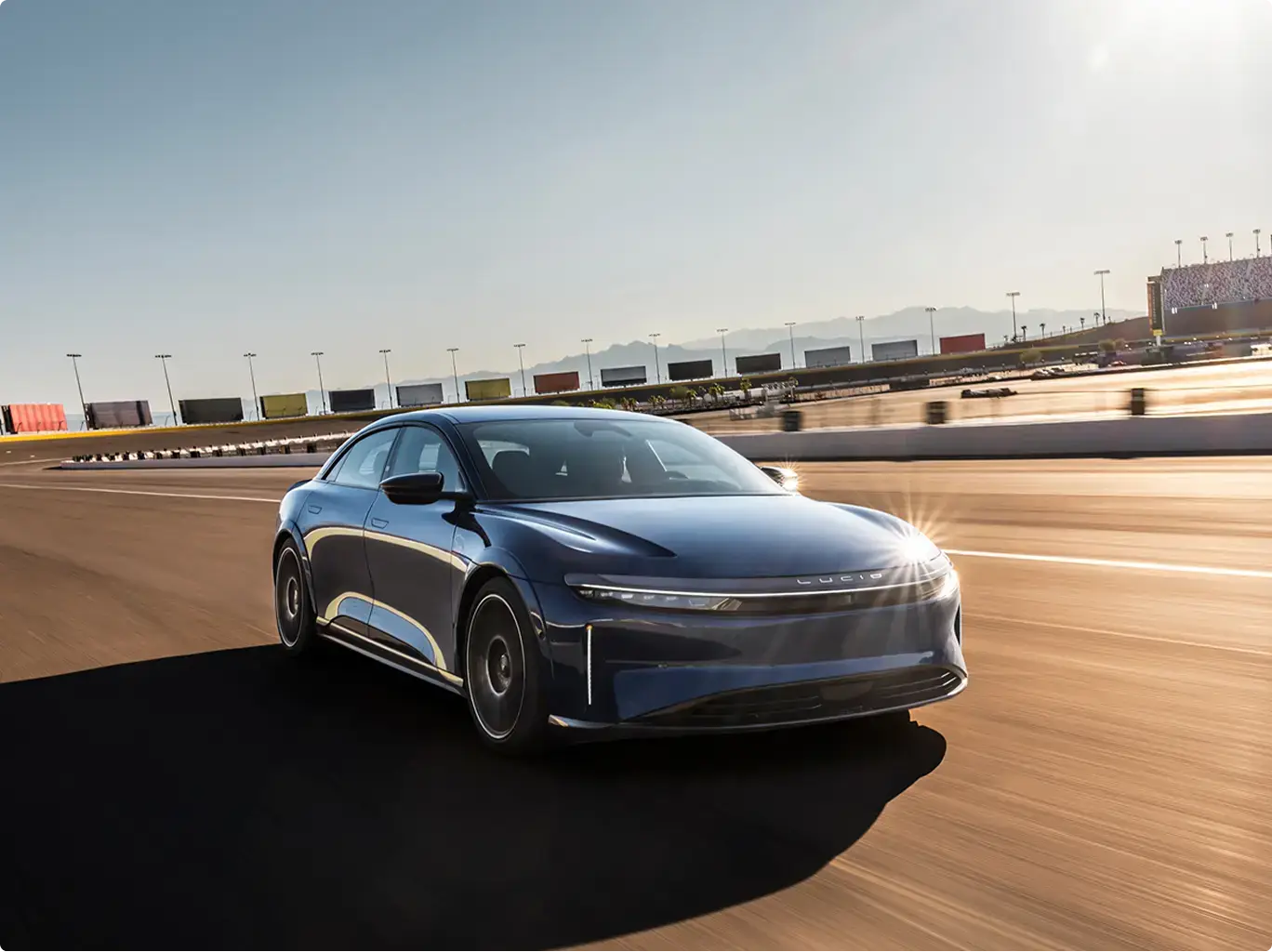 Lucid Air Sapphire speeding on a racetrack with mountains visible in the background under clear sky.