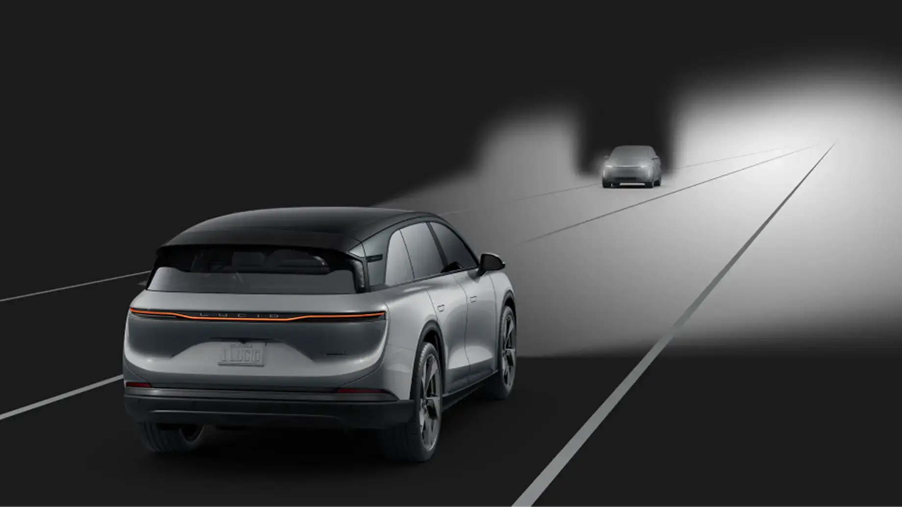 Rear view of a silver Lucid electric SUV on a dark road, headlights illuminating an oncoming car ahead.