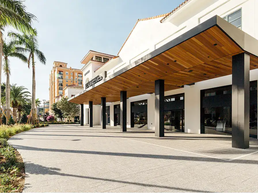 Lucid Motors showroom exterior with wood-paneled canopy, black columns, white facade, palm trees, and a hotel building in the background.