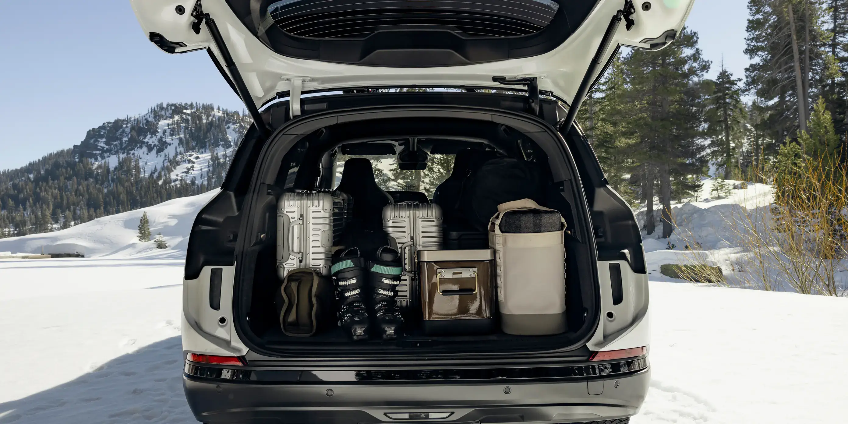 Lucid Gravity with open trunk packed with ski gear and luggage against snowy mountain backdrop.