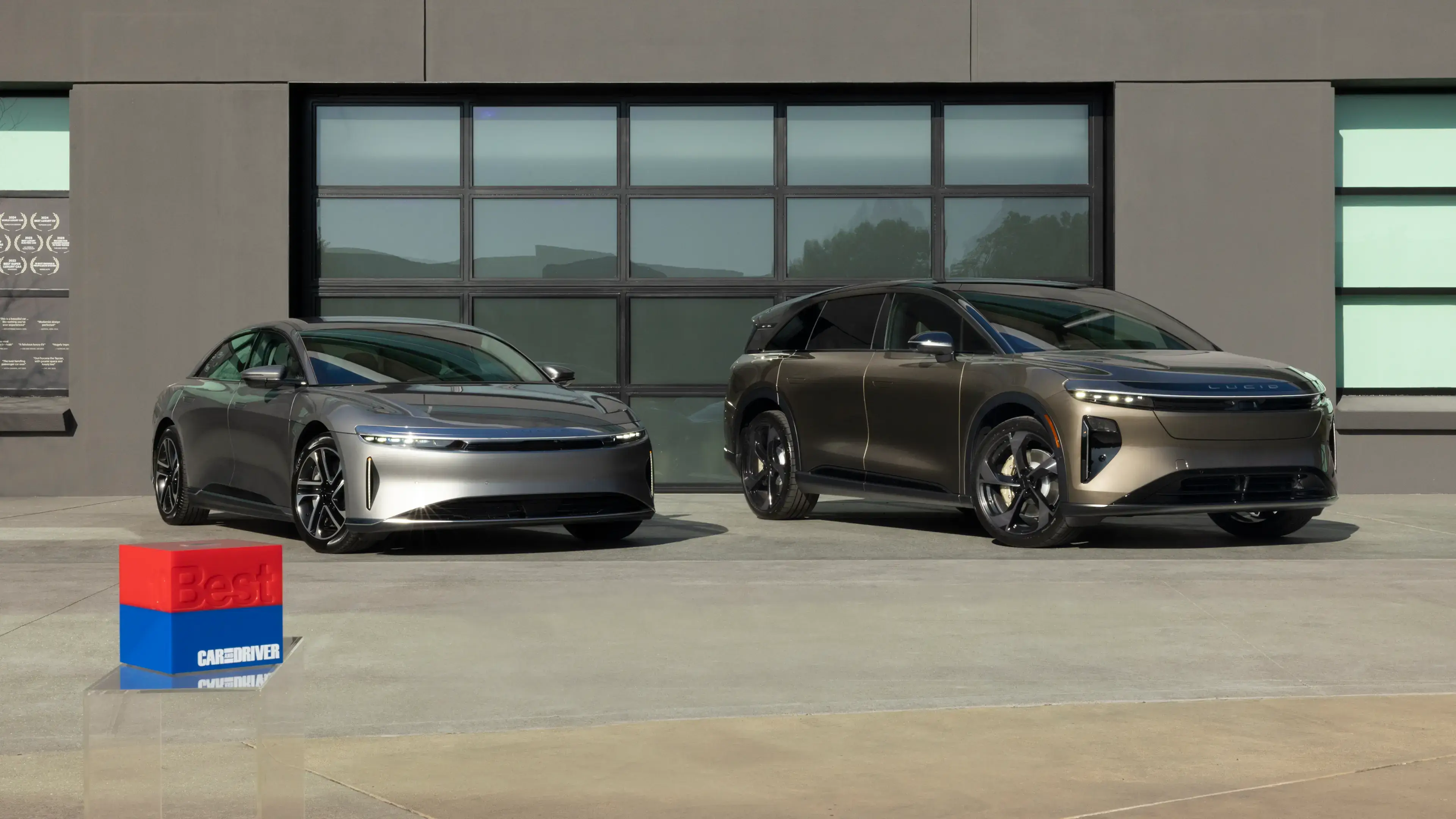سيارتا Lucid Air وLucid Gravity متوقفتان أمام صالة عرض عصرية، مع مجسم جائزة أفضل 10 سيارات من كار أند درايفر في المقدمة.