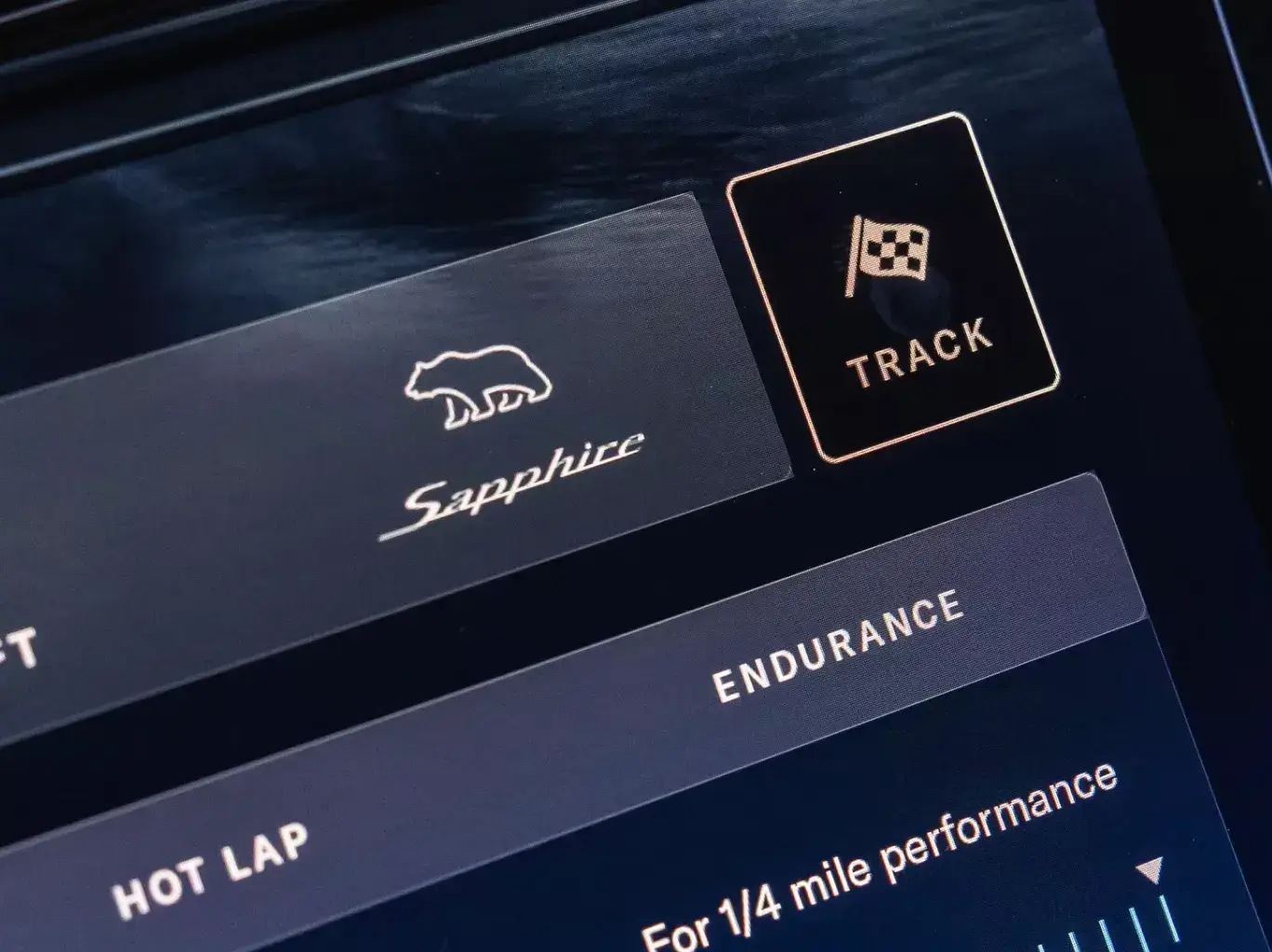 Close-up of car dashboard display showing driving modes including Sapphire, Track, and Endurance with a checkered flag icon.