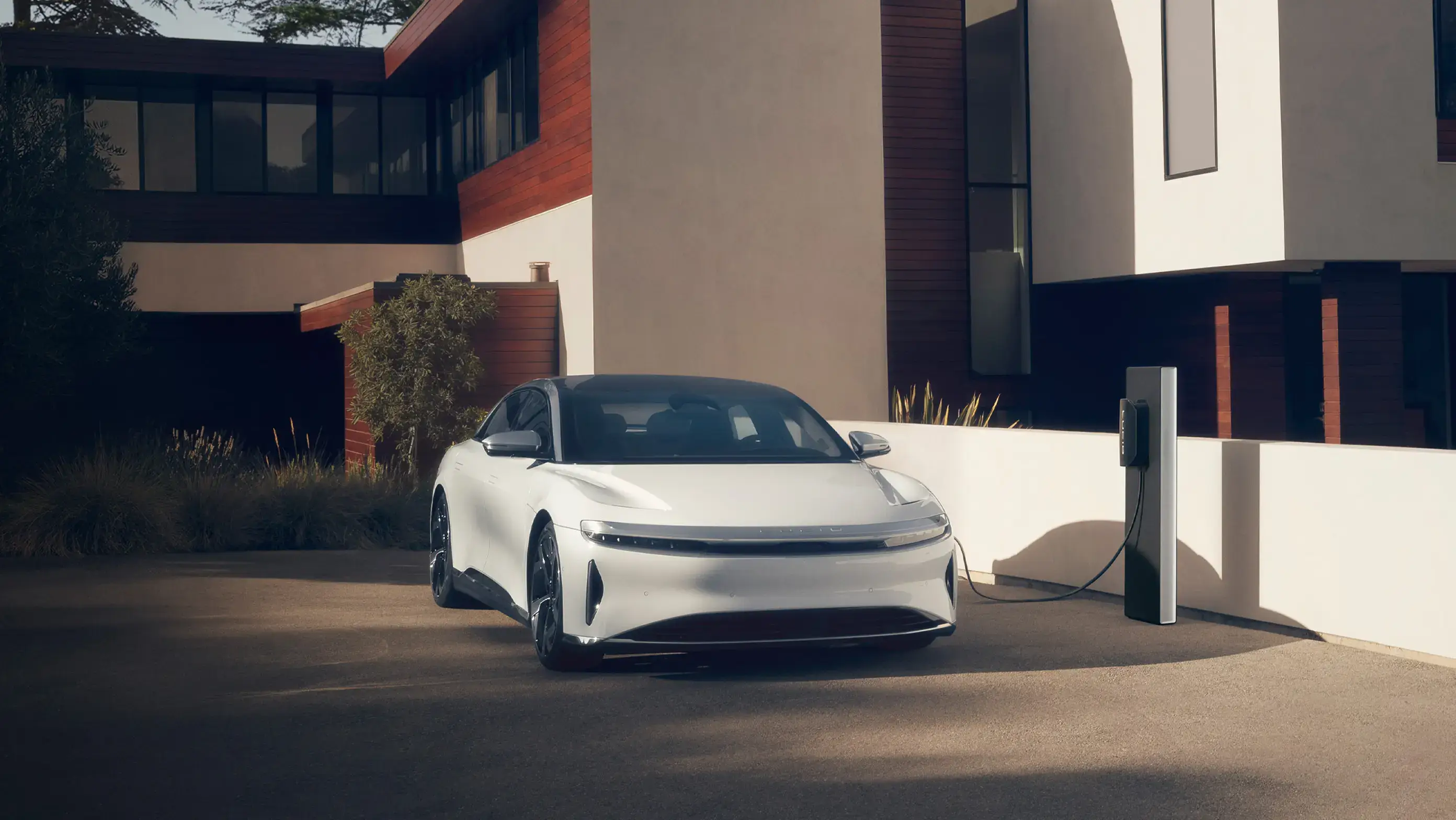 White electric car charging at a modern home with wood and white exterior, sleek architecture in background.