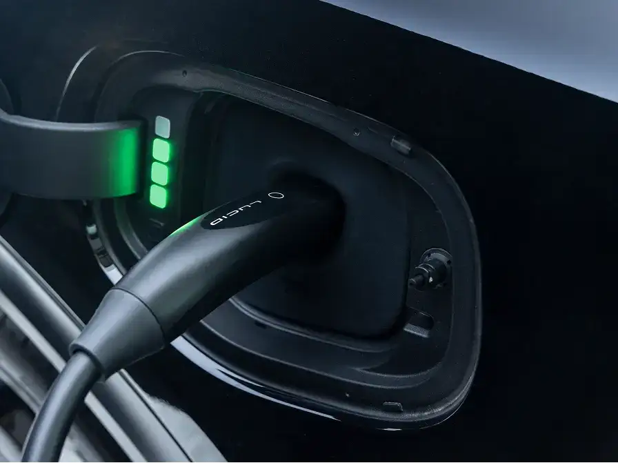 A Lucid electric vehicle charging port with a black cable plugged in and green indicator lights showing active charging.