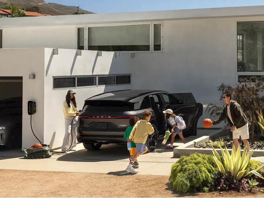 A family outside a modern home with a black Lucid Gravity SUV charging, children playing with a basketball in the driveway.