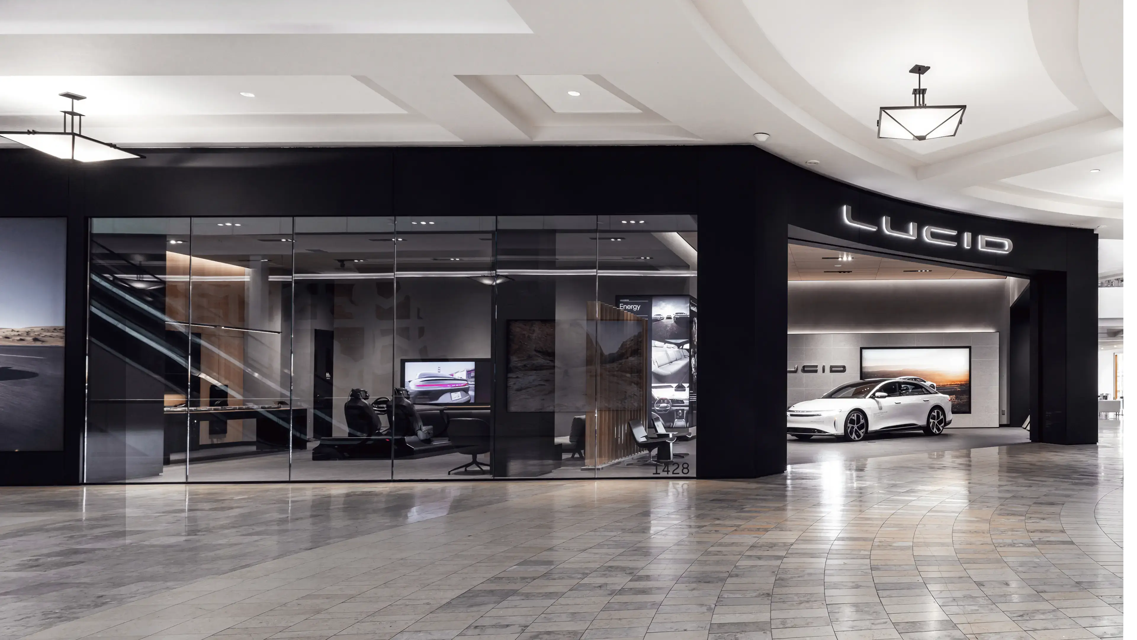 Modern Lucid Motors studio with sleek white electric sedan displayed under illuminated signage in upscale mall setting.