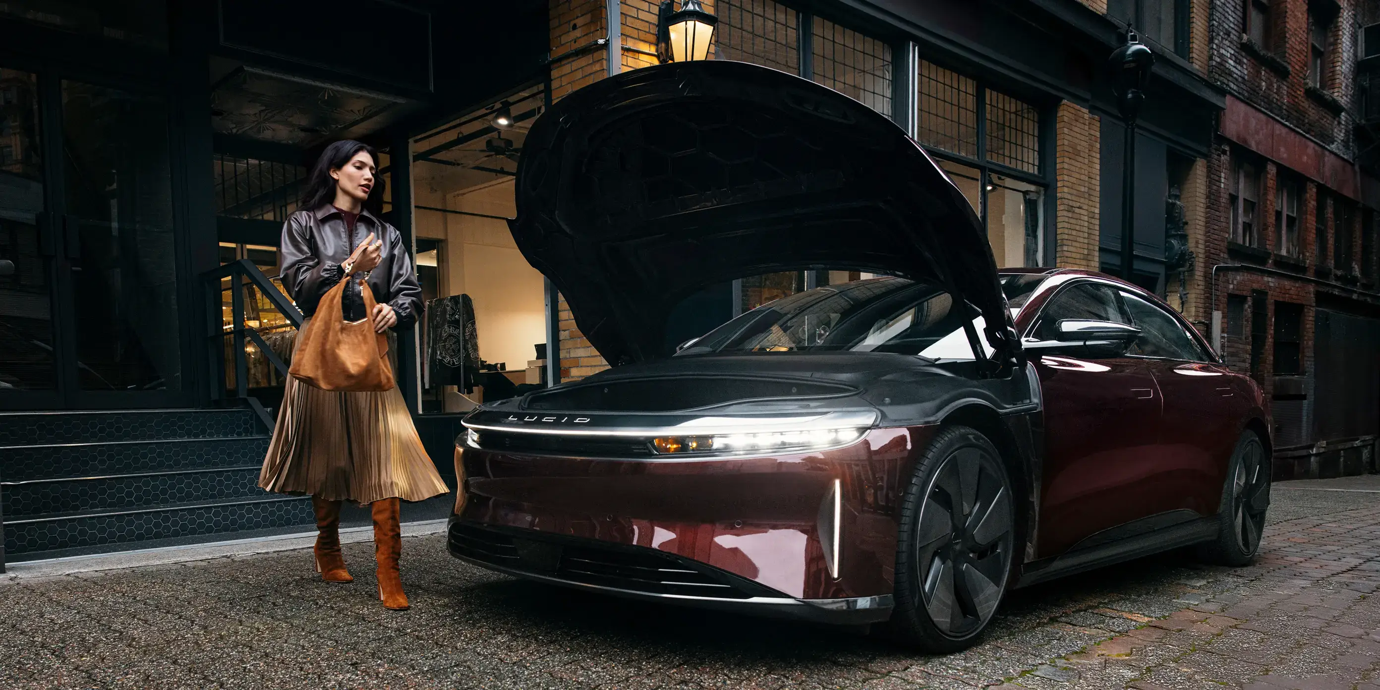 Zenith Red Lucid Air with open hood parked on city street at dusk, person with leather bag nearby.