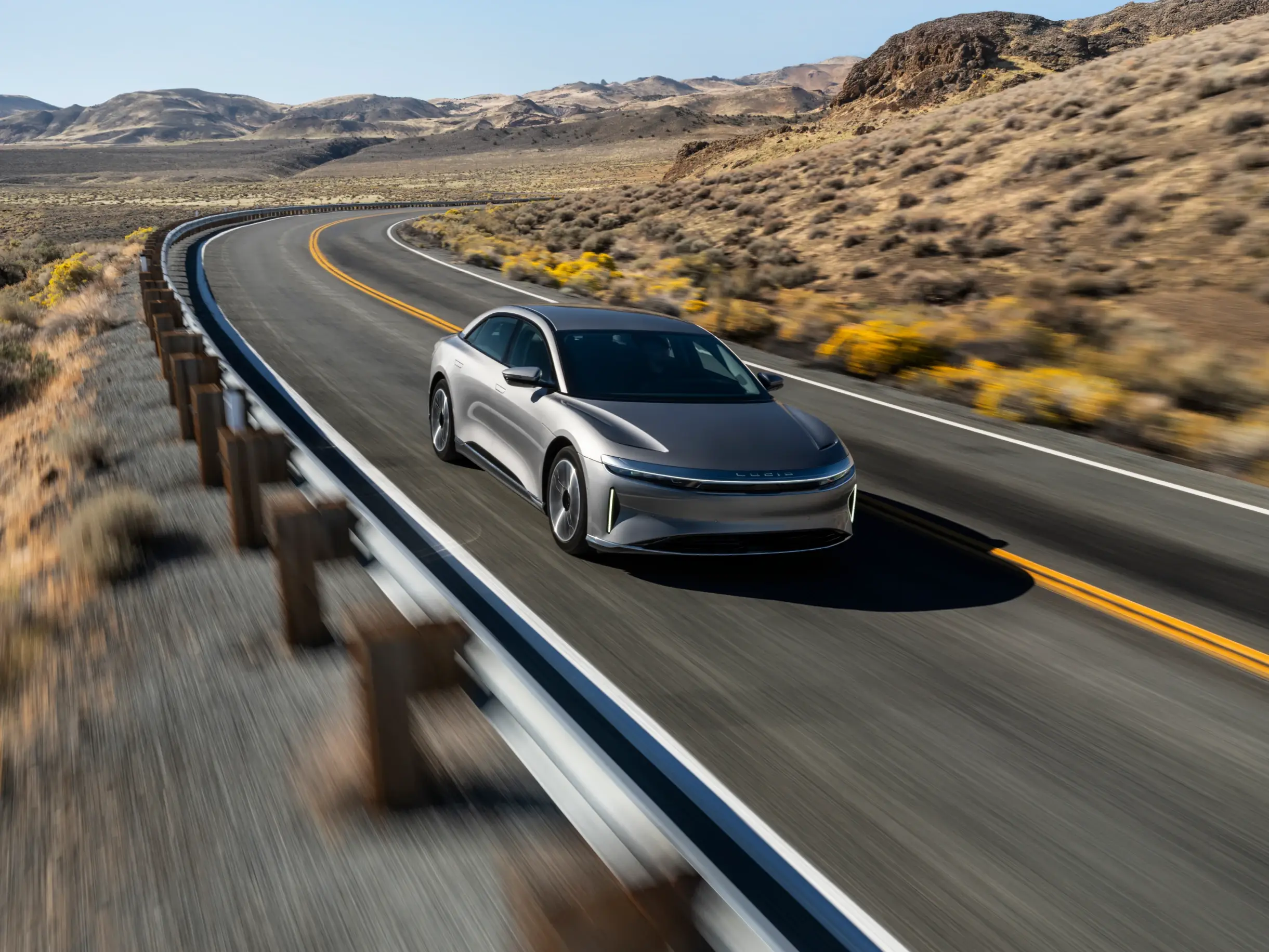 Eine Lucid Air, die bei Sonnenuntergang auf einer kurvigen Wüstenstrasse fährt, mit felsigen Hügeln im Hintergrund.