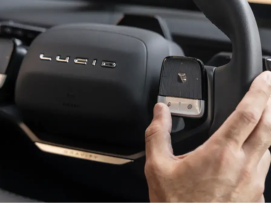 Close-up of a hand operating controls on a Lucid vehicle's steering wheel with the Lucid logo visible on the airbag cover.