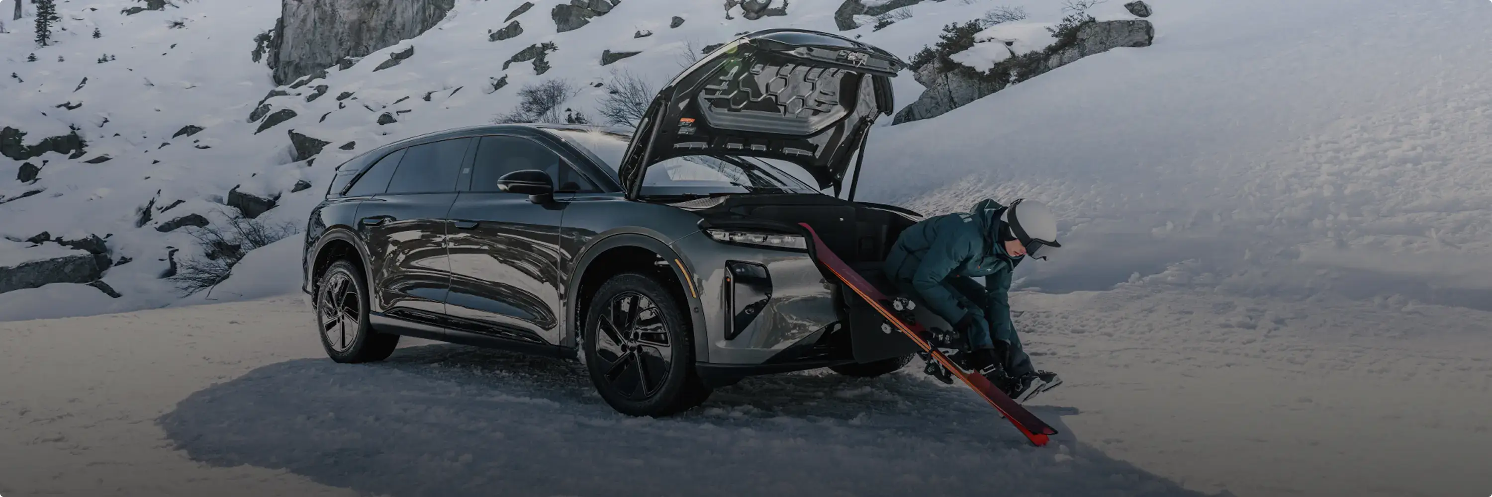 Skier preparing equipment beside silver SUV with open trunk in snowy mountain landscape