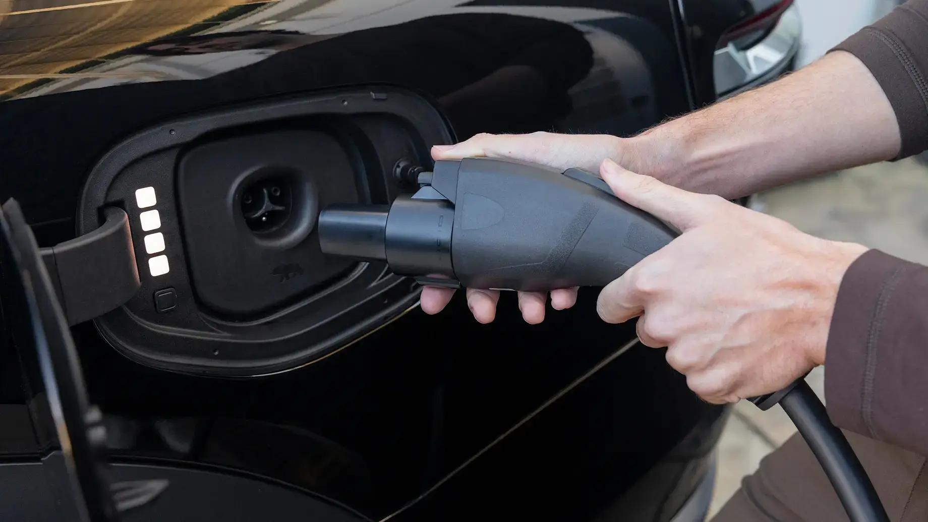 Hands plugging a charging cable into an electric vehicle's charging port on a black car.