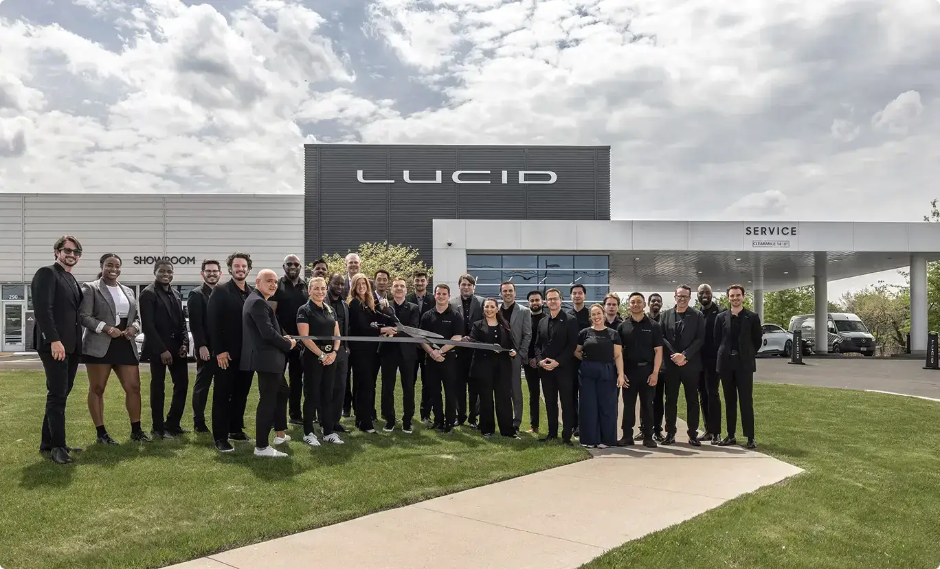 Team gathered for ribbon-cutting ceremony outside Lucid Motors showroom and service center under cloudy sky.