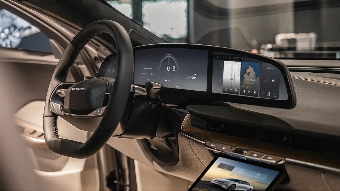 Lucid Air car interior featuring a black steering wheel and a wide curved digital dashboard display with navigation.