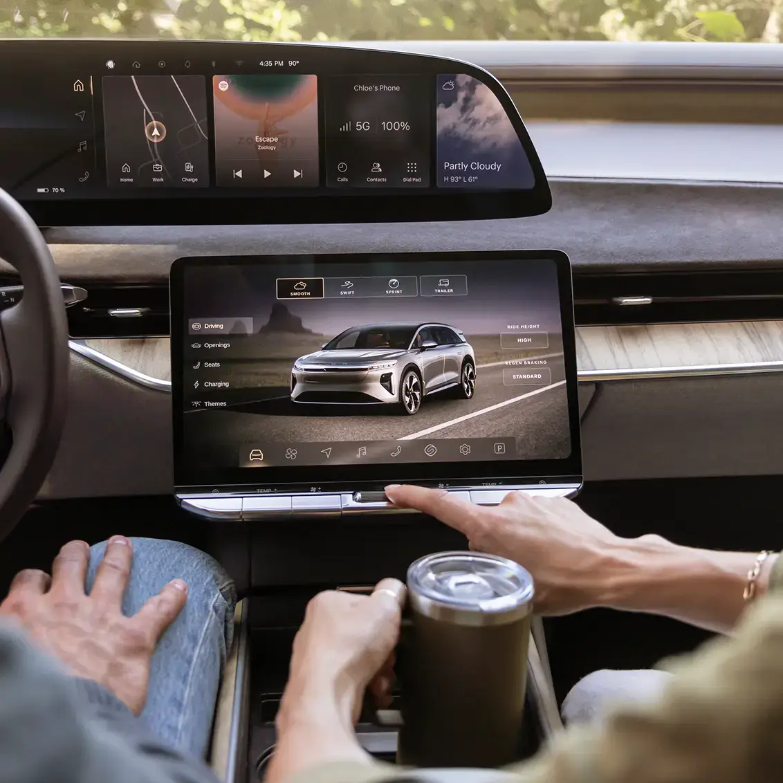 Modern car interior with dual touchscreens showing music interface and vehicle settings, with a hand touching the display.