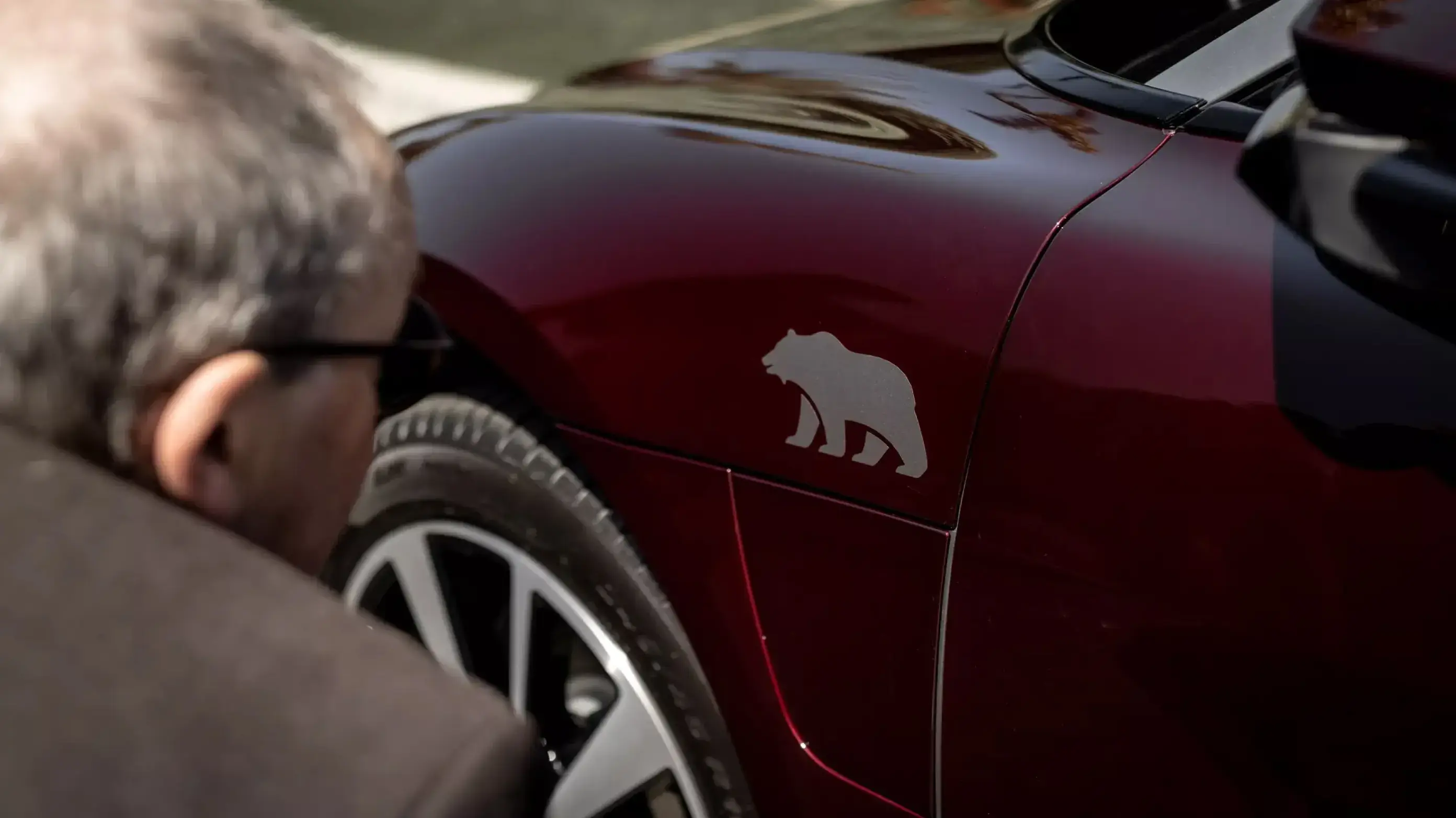 Close-up of a Lucid Air with a silver bear silhouette logo on its side panel, with a person partially visible.