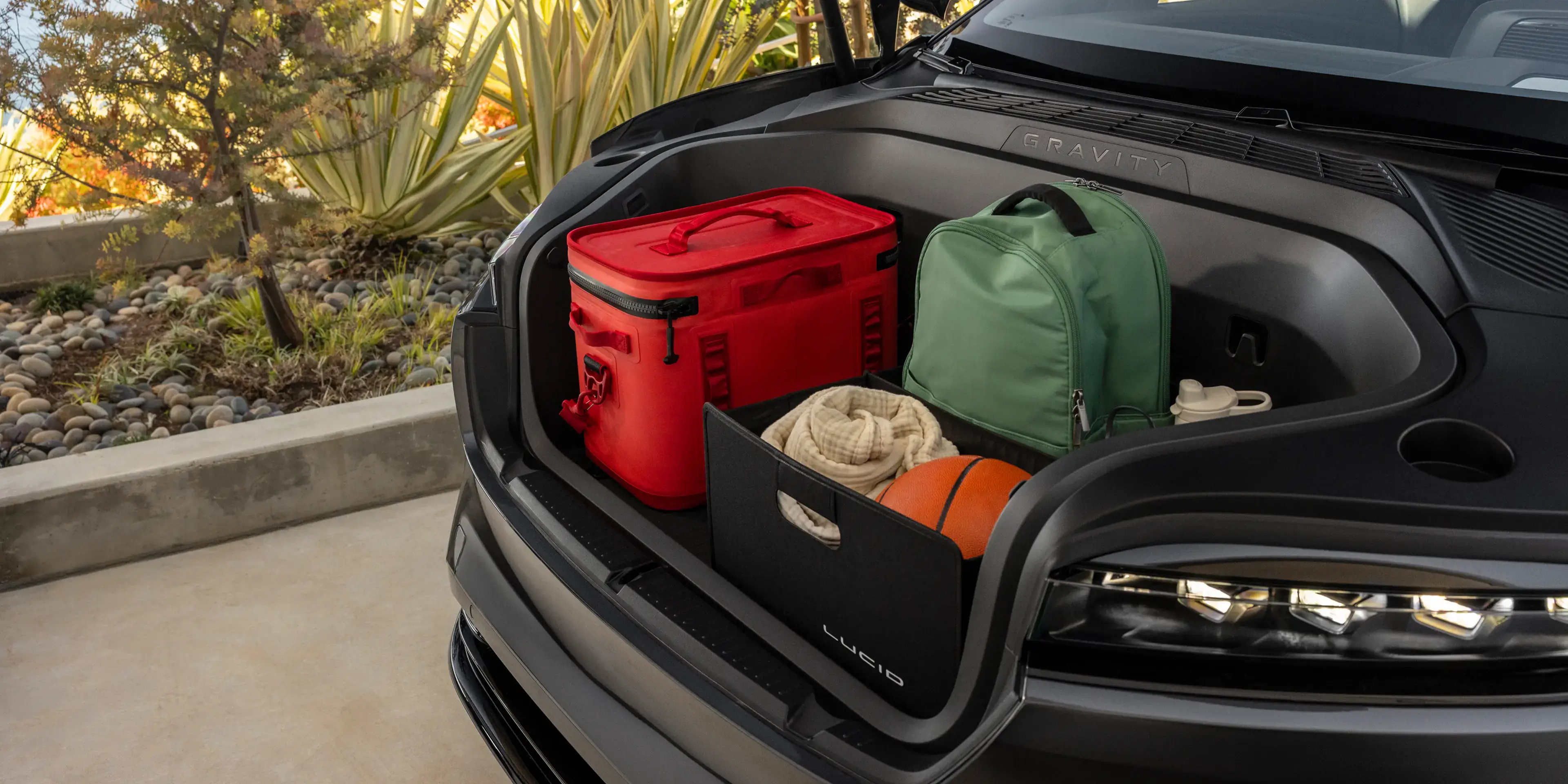 Open trunk of a Lucid Gravity SUV loaded with a red cooler, green bag, blanket, and basketball.