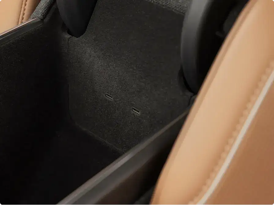 Close-up of a car interior storage compartment with black carpet lining and tan leather trim visible on the edges.