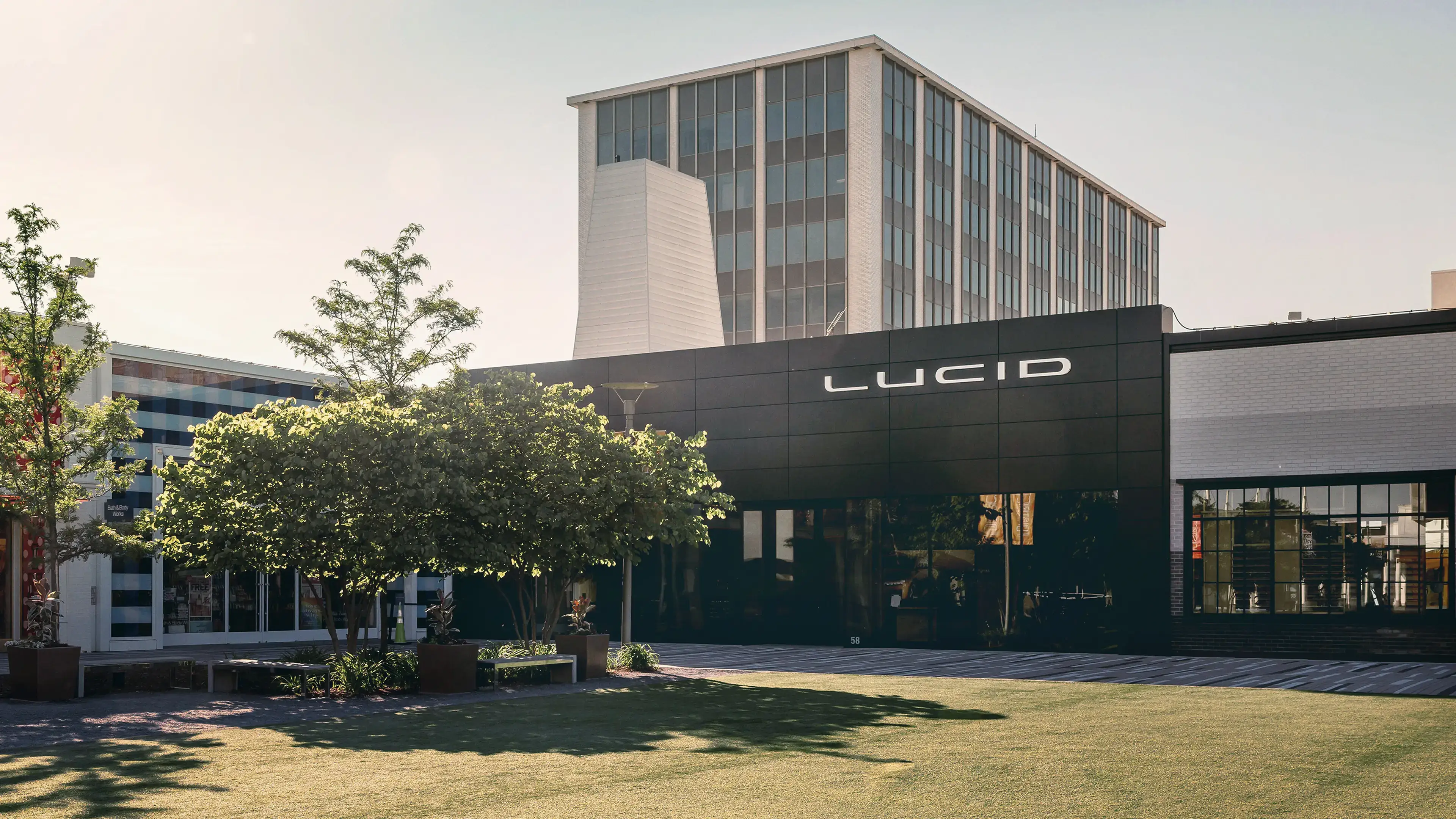 Lucid Motors studio with modern black entrance facade and glass office building behind it on a sunny day.