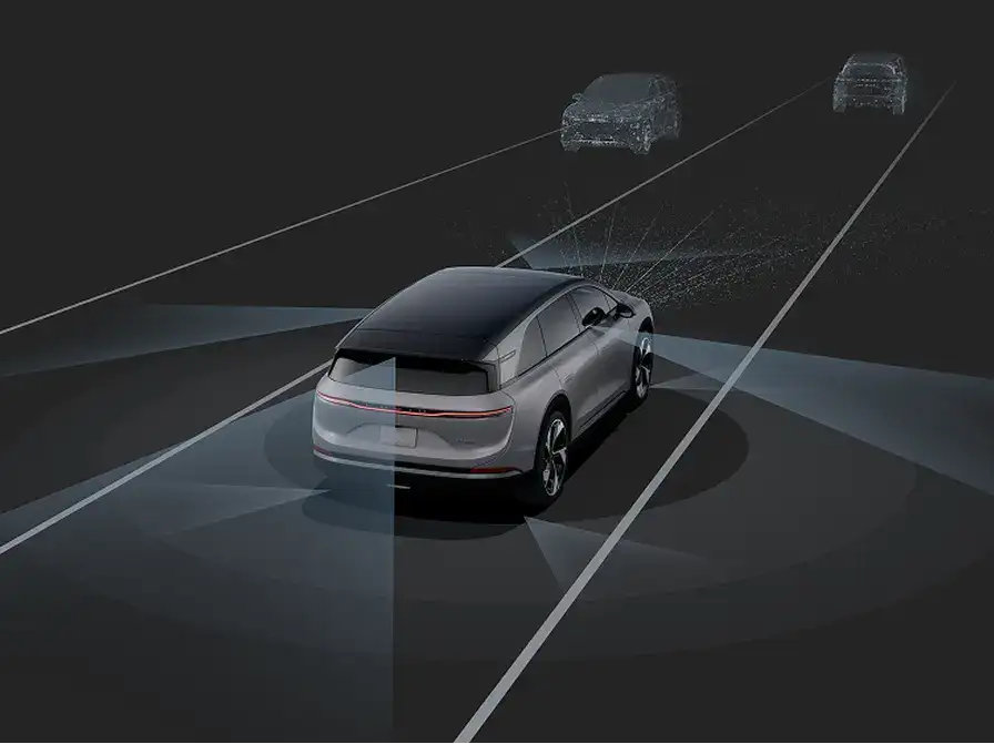A silver electric vehicle on a dark road with sensor beams detecting two cars ahead, illustrating autonomous driving technology.