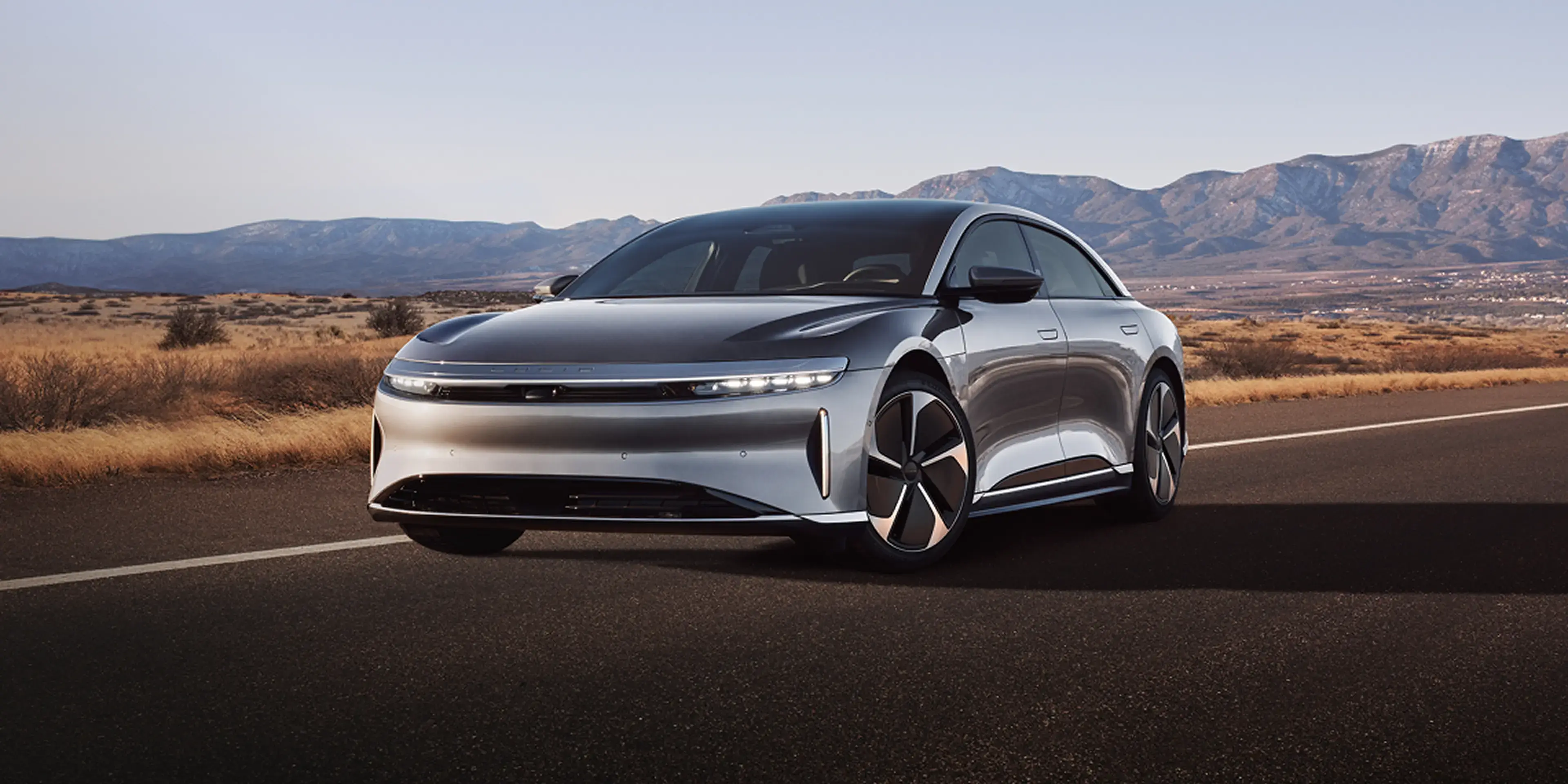 Lucid Air on desert road with mountains in background under clear sky.