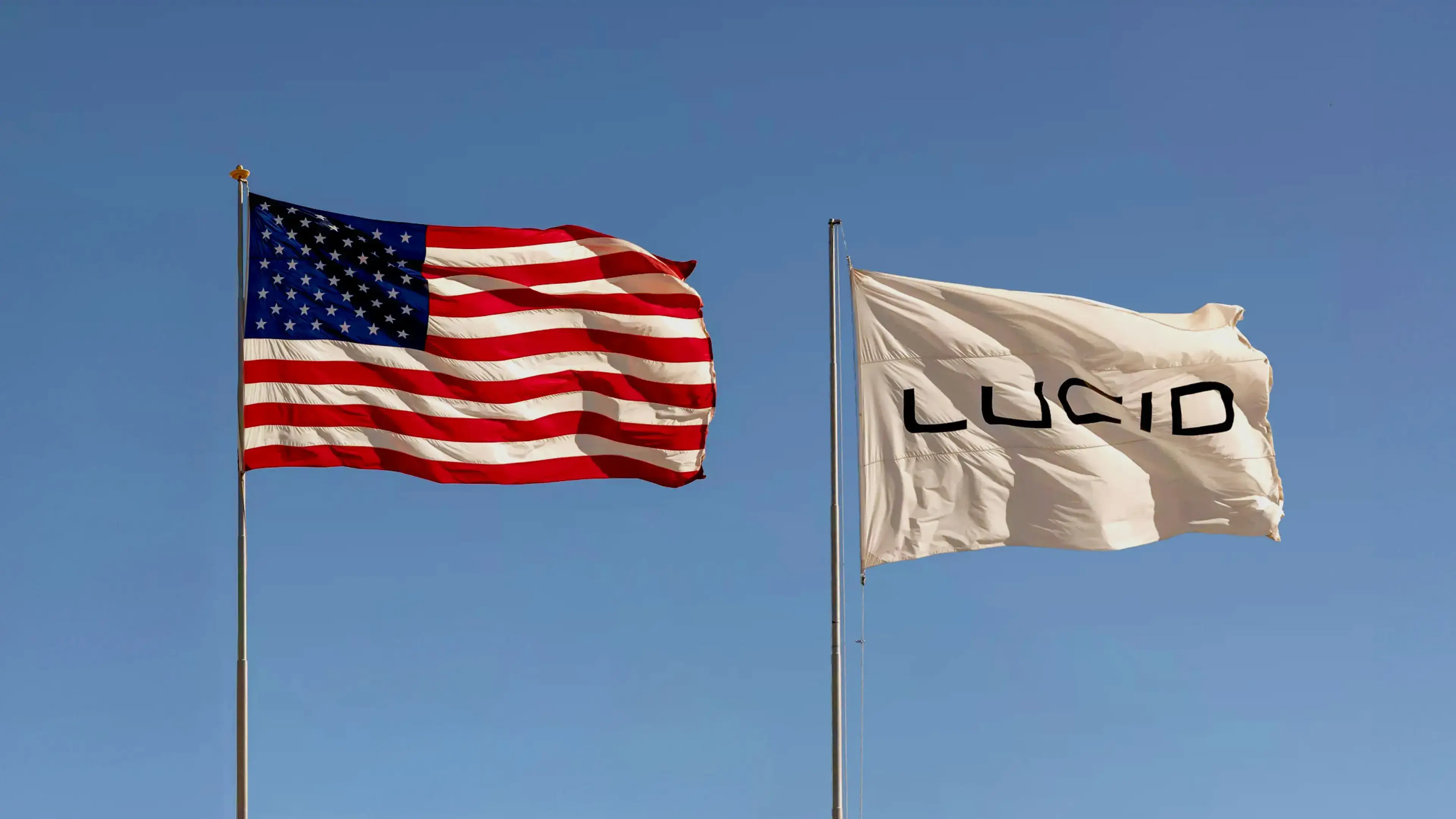 American flag and white Lucid company flag waving side by side against a clear blue sky.