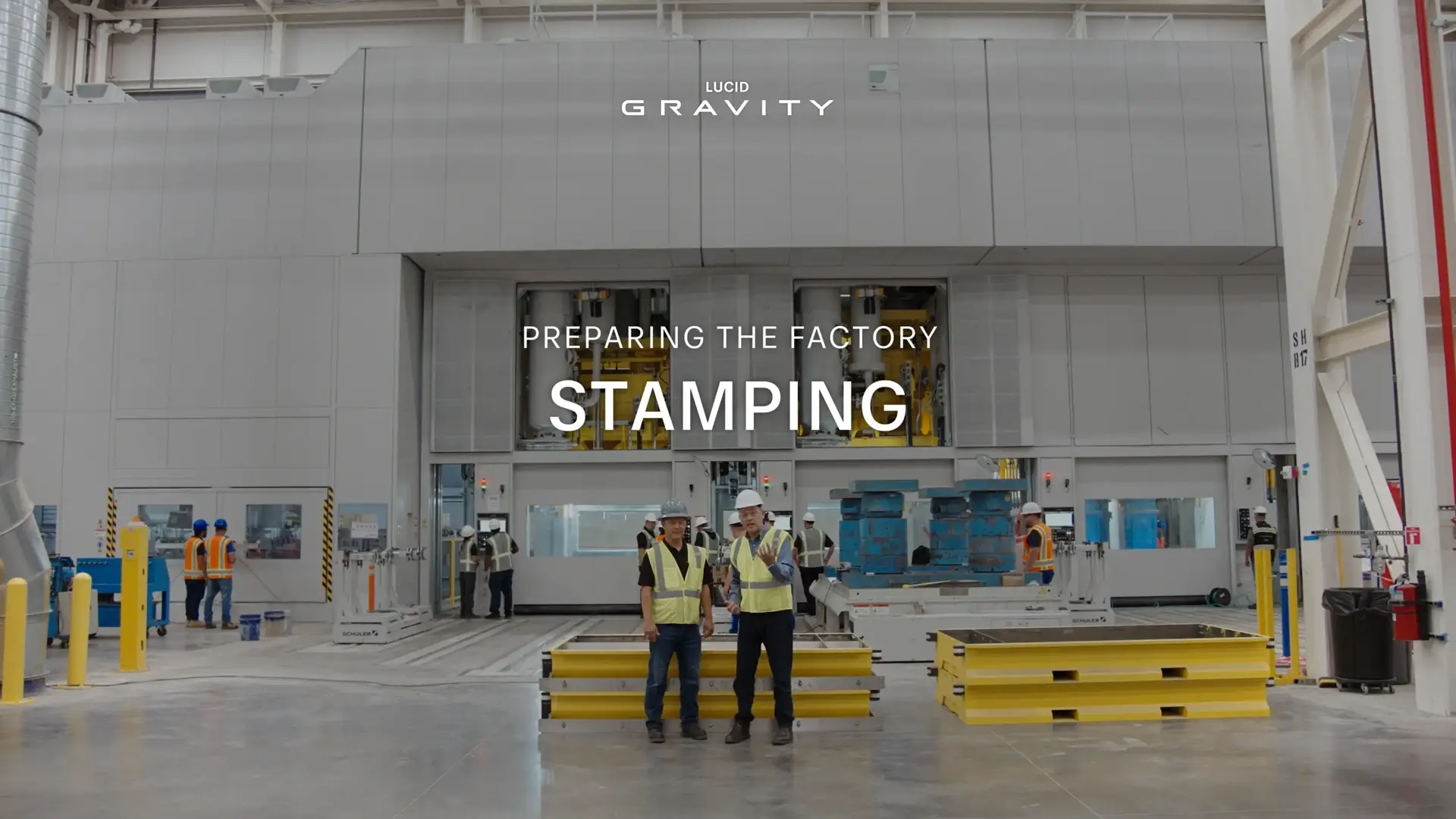Workers in safety gear inside Lucid Gravity factory stamping area with "PREPARING THE FACTORY STAMPING" text overlay.