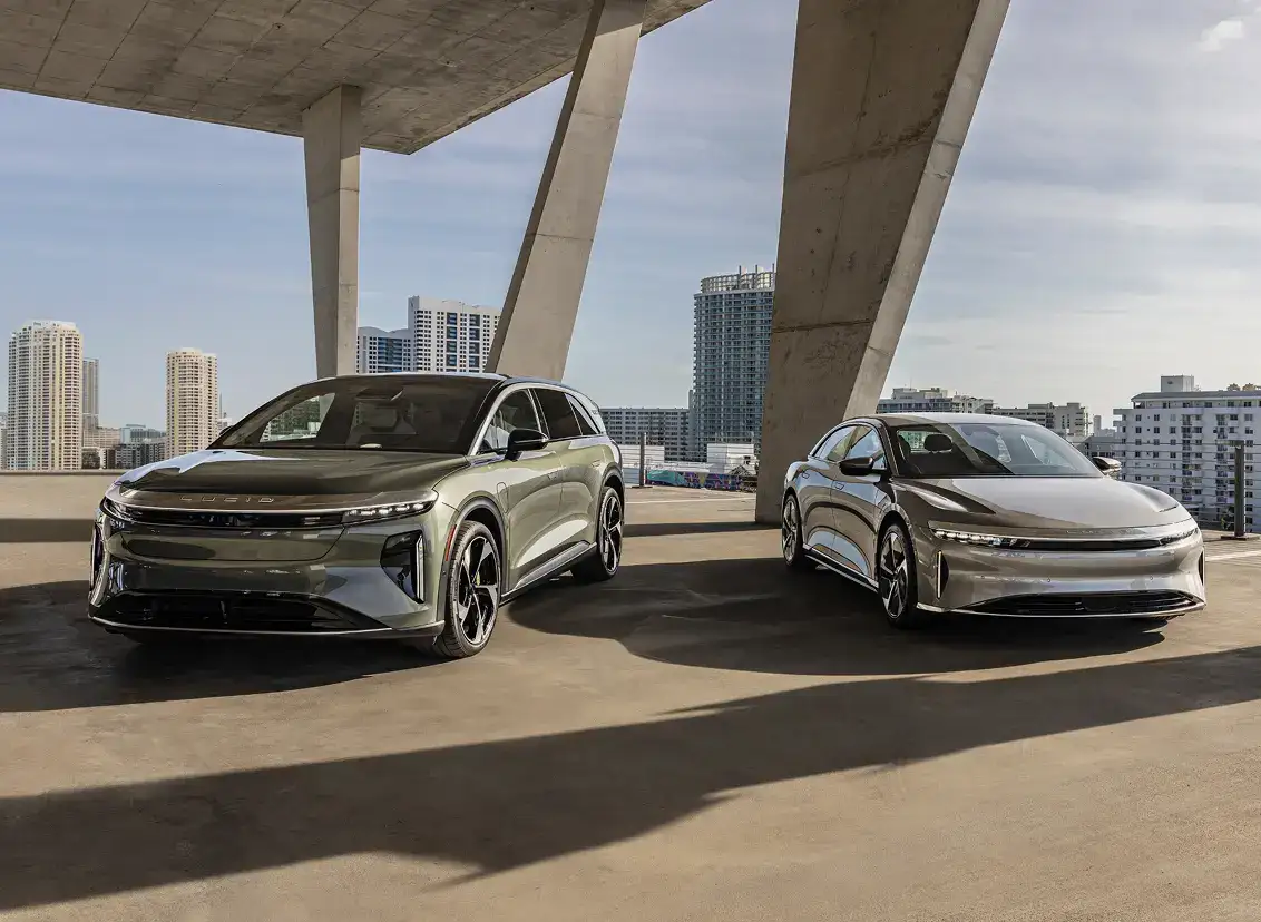 Two Lucid electric vehicles—an SUV and a sedan—parked on a rooftop with a city skyline in the background.