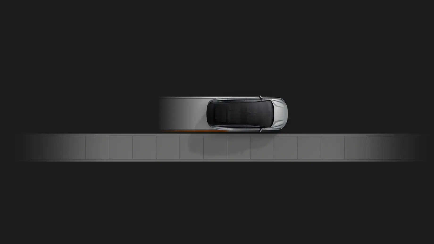 Aerial top-down view of a silver SUV with a black roof on a gray surface against a dark background.