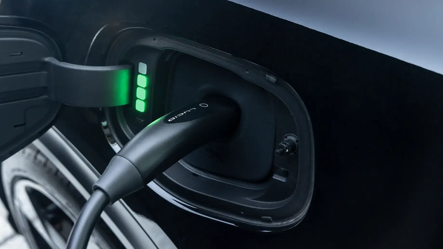 Electric vehicle charging port with black charging cable plugged in, showing green indicator lights for battery status.