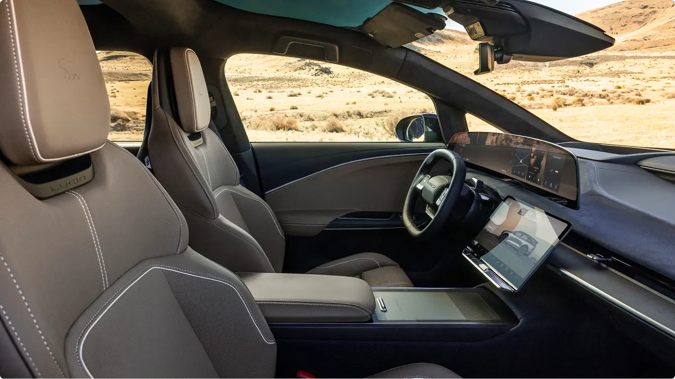 Luxury electric vehicle interior with gray leather seats, digital displays, and desert landscape visible through windows.