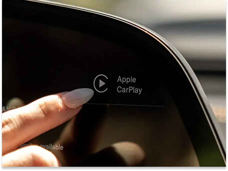 Finger touching a car dashboard display showing Apple CarPlay interface with play button icon