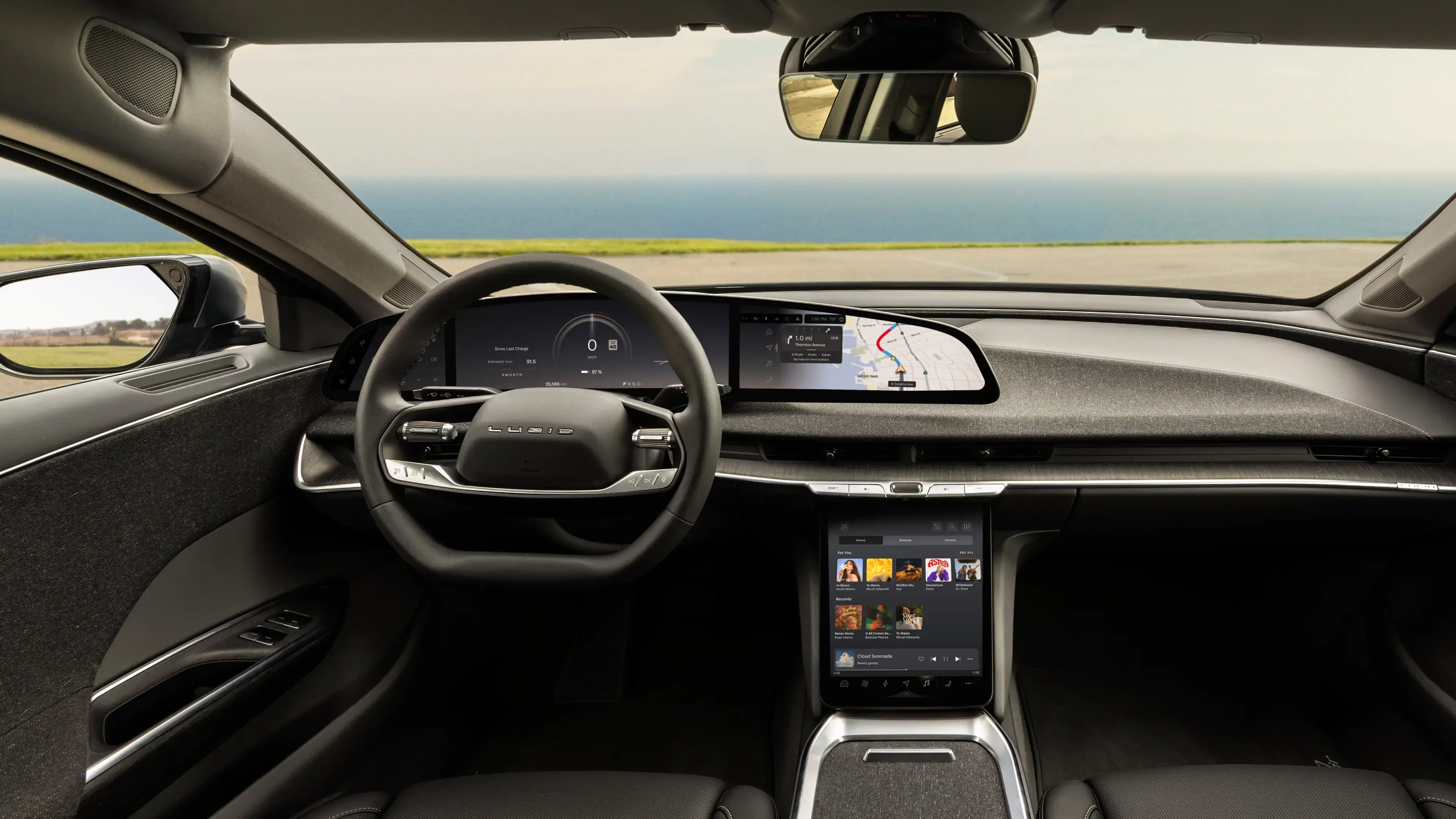 Lucid Air interior with steering wheel, wide dashboard display showing navigation, and center touchscreen with music app.