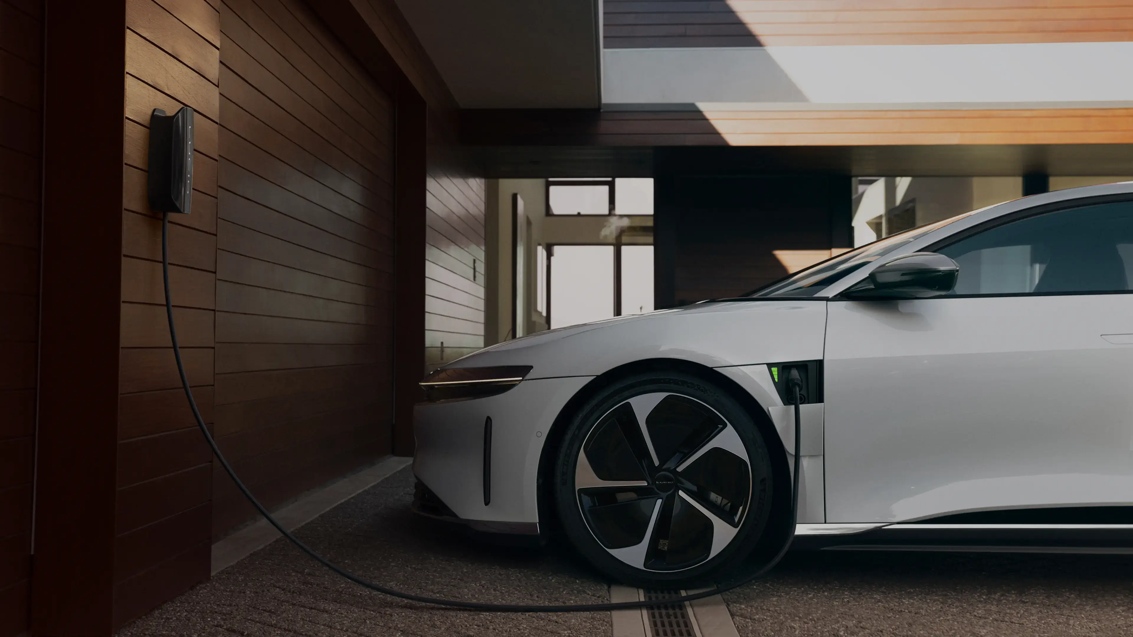 White electric car charging in a modern garage with wooden wall panels and a wall-mounted charging station.