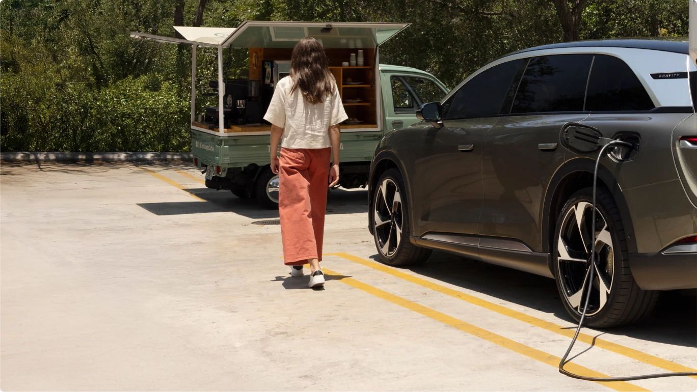 Person in orange pants walking past an electric vehicle charging, with a mobile café truck in the background.