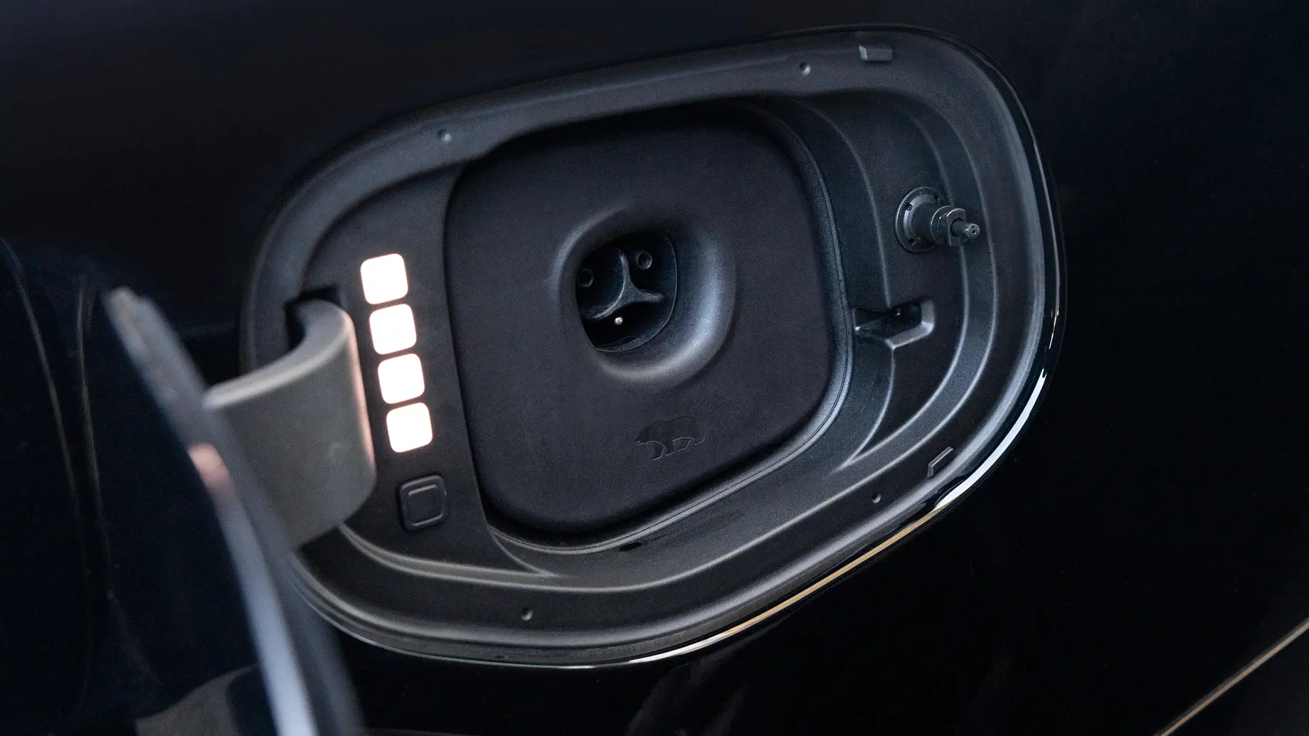 Close-up of an electric vehicle charging port with illuminated indicator lights on the open flap door.
