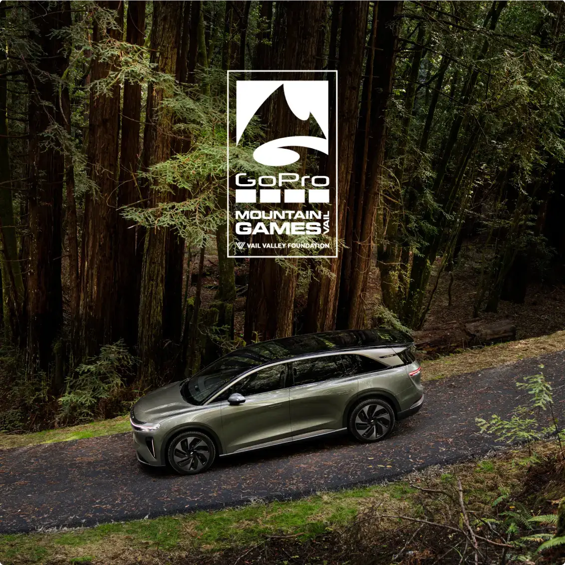 A Lucid Gravity SUV on a forest road with the GoPro Mountain Games Vail Valley Foundation logo overhead.