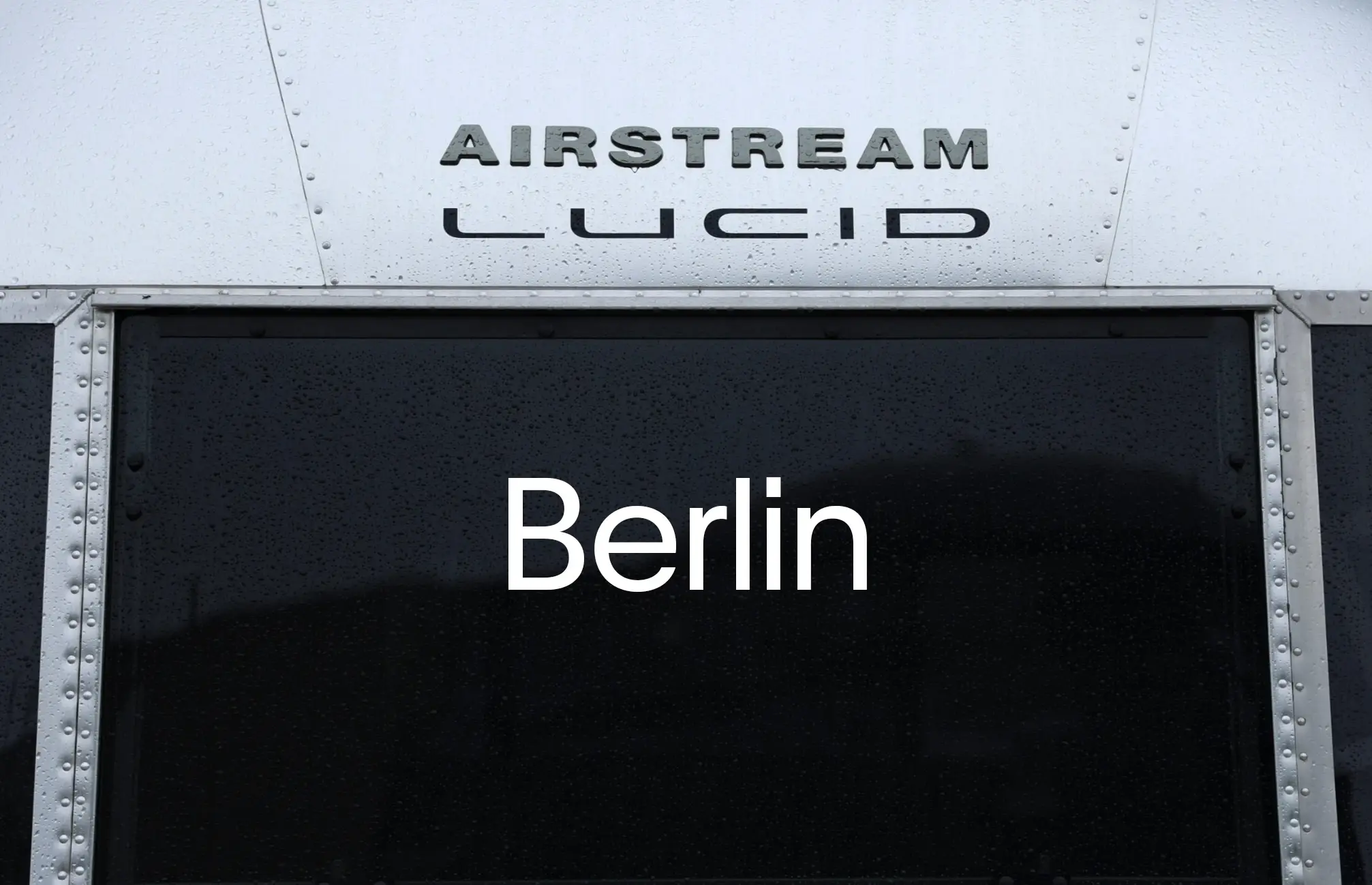 Gros plan sur un panneau métallique de style Airstream avec les inscriptions en relief « AIRSTREAM » et « LUCID », et « Berlin » affiché sur le panneau sombre en dessous.
