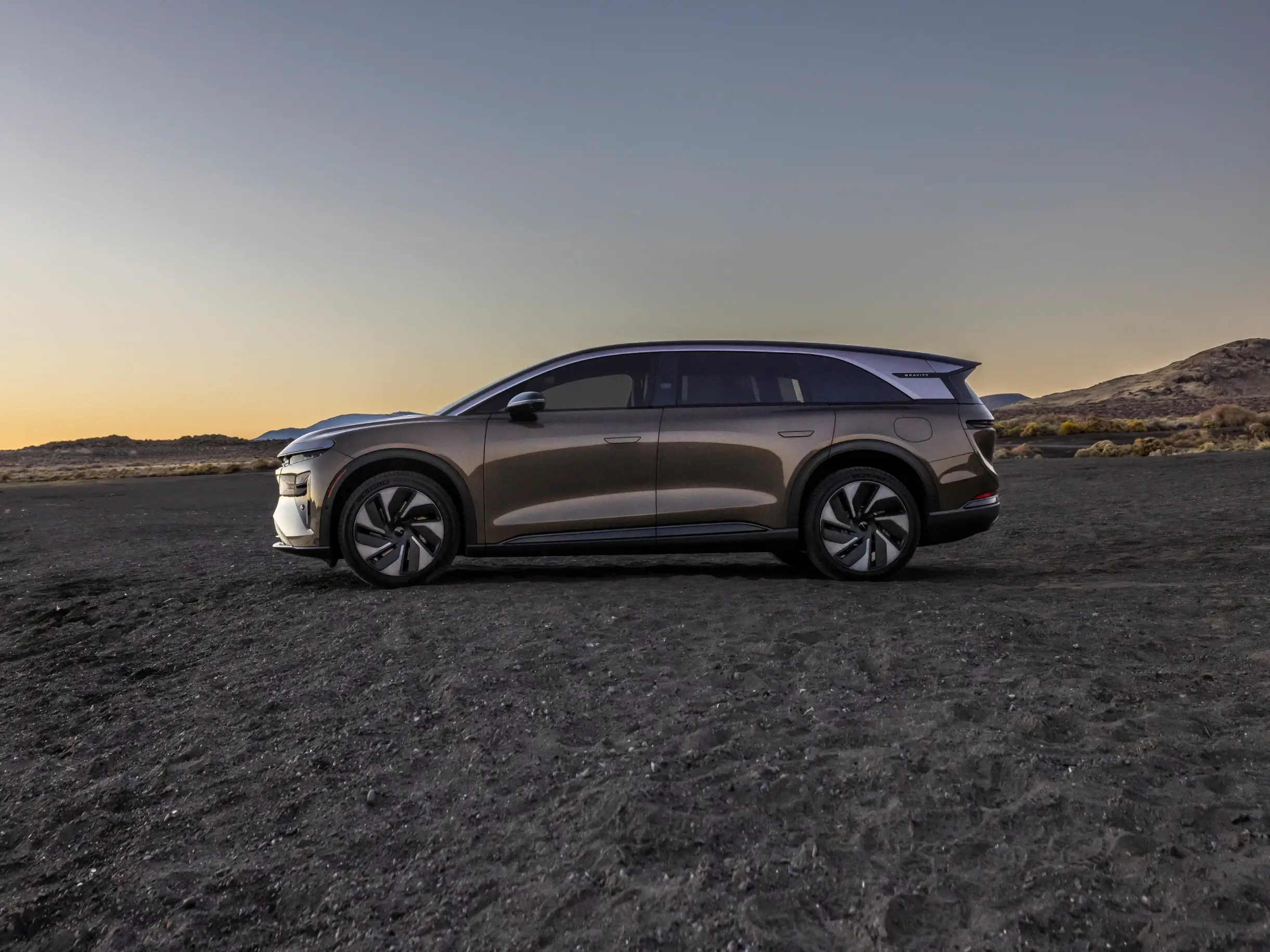 Een Lucid Gravity staat geparkeerd in open terrein tijdens zonsondergang, waarbij het strakke ontwerp wordt benadrukt tegen de glooiende heuvels.