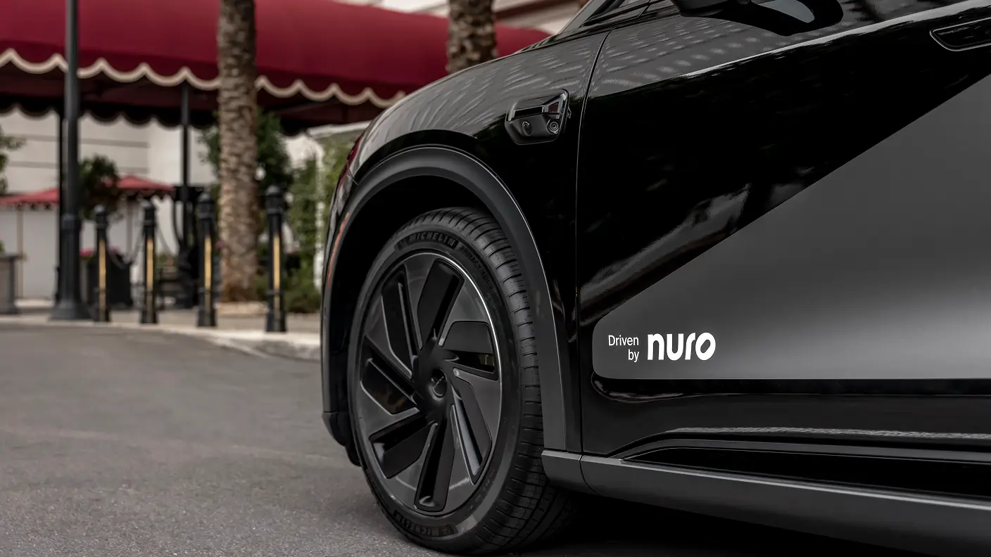 Close-up of a sleek black vehicle with “Driven by Nuro” logo on its side, parked near a building with red awnings.