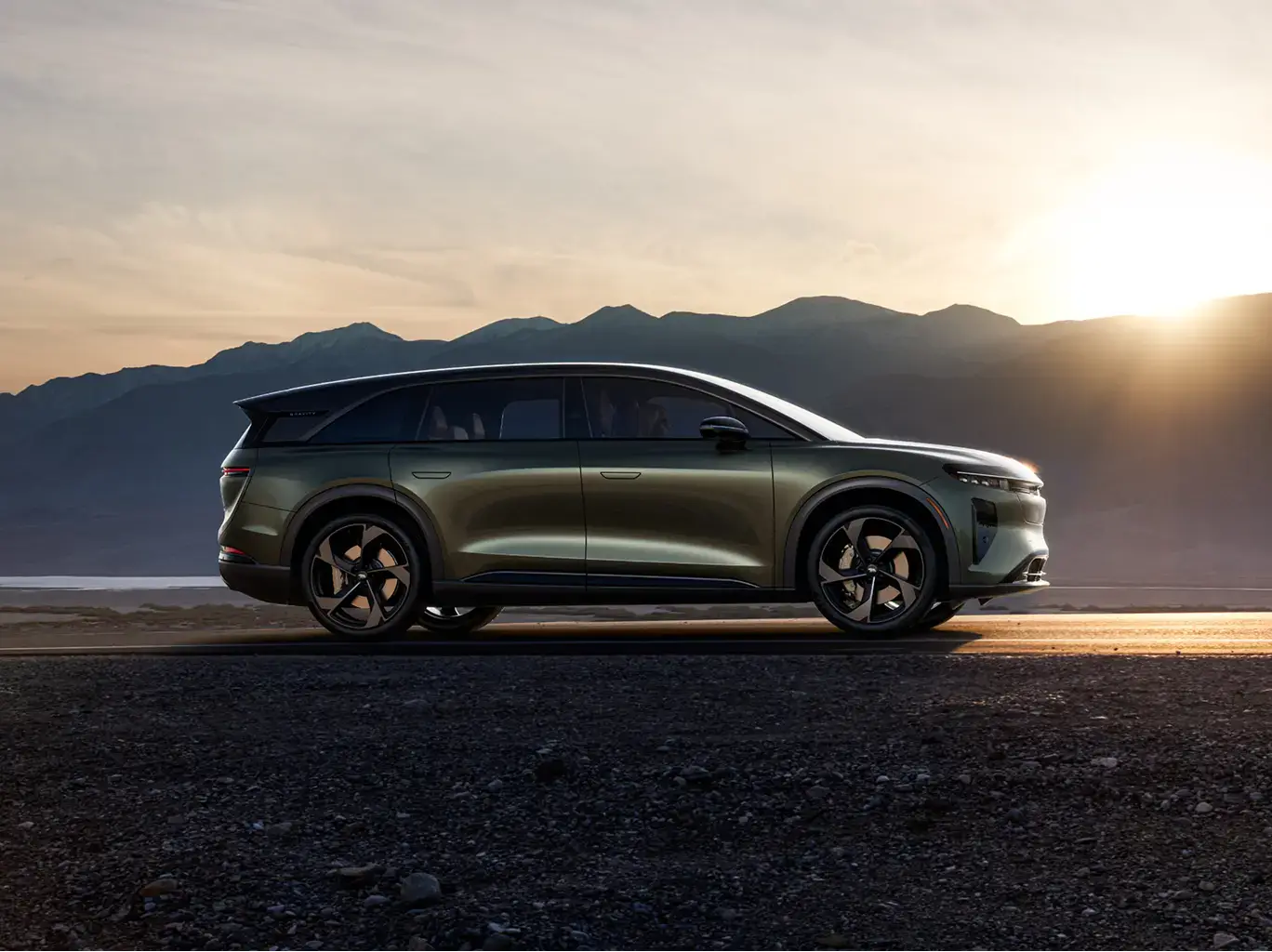 Lucid Gravity in Aurora Green parked on rocky terrain at sunset with mountain silhouettes in the background.