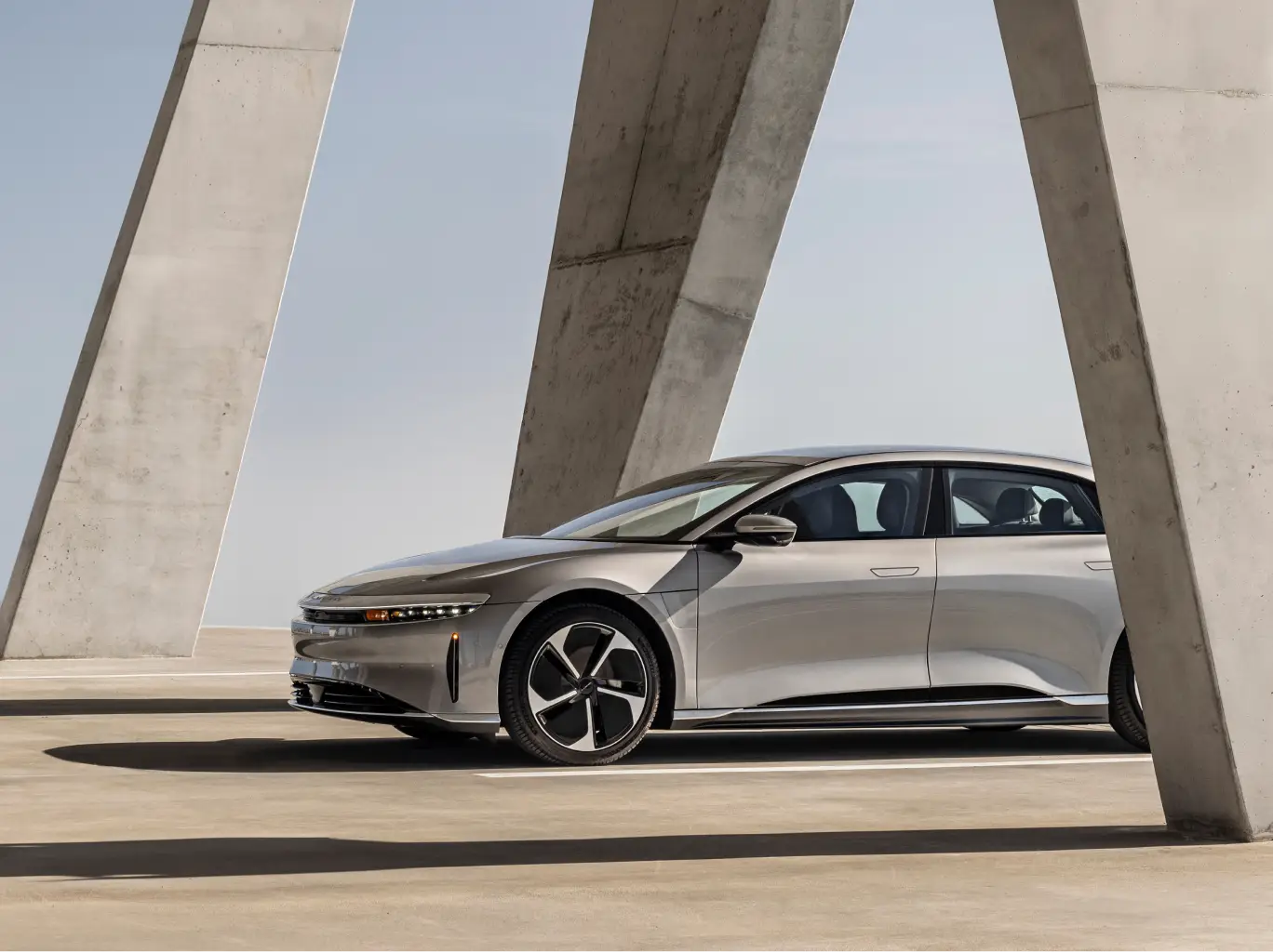 Sleek Lucid Air sedan parked beneath angular concrete architecture, featuring modern design and black accent wheels.